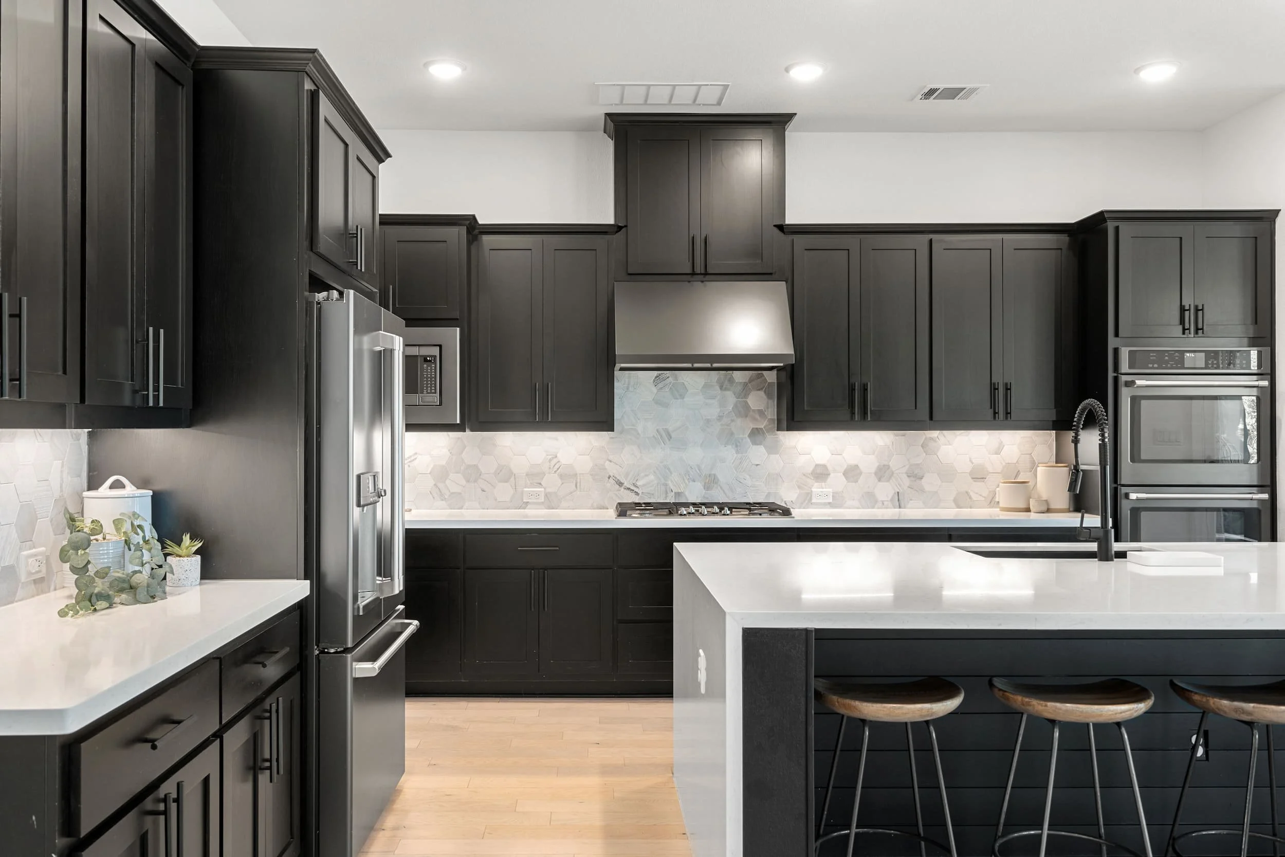 Austin kitchen staging with black cabinets, quartz island, hex tile backsplash, wood stools, modern lighting.