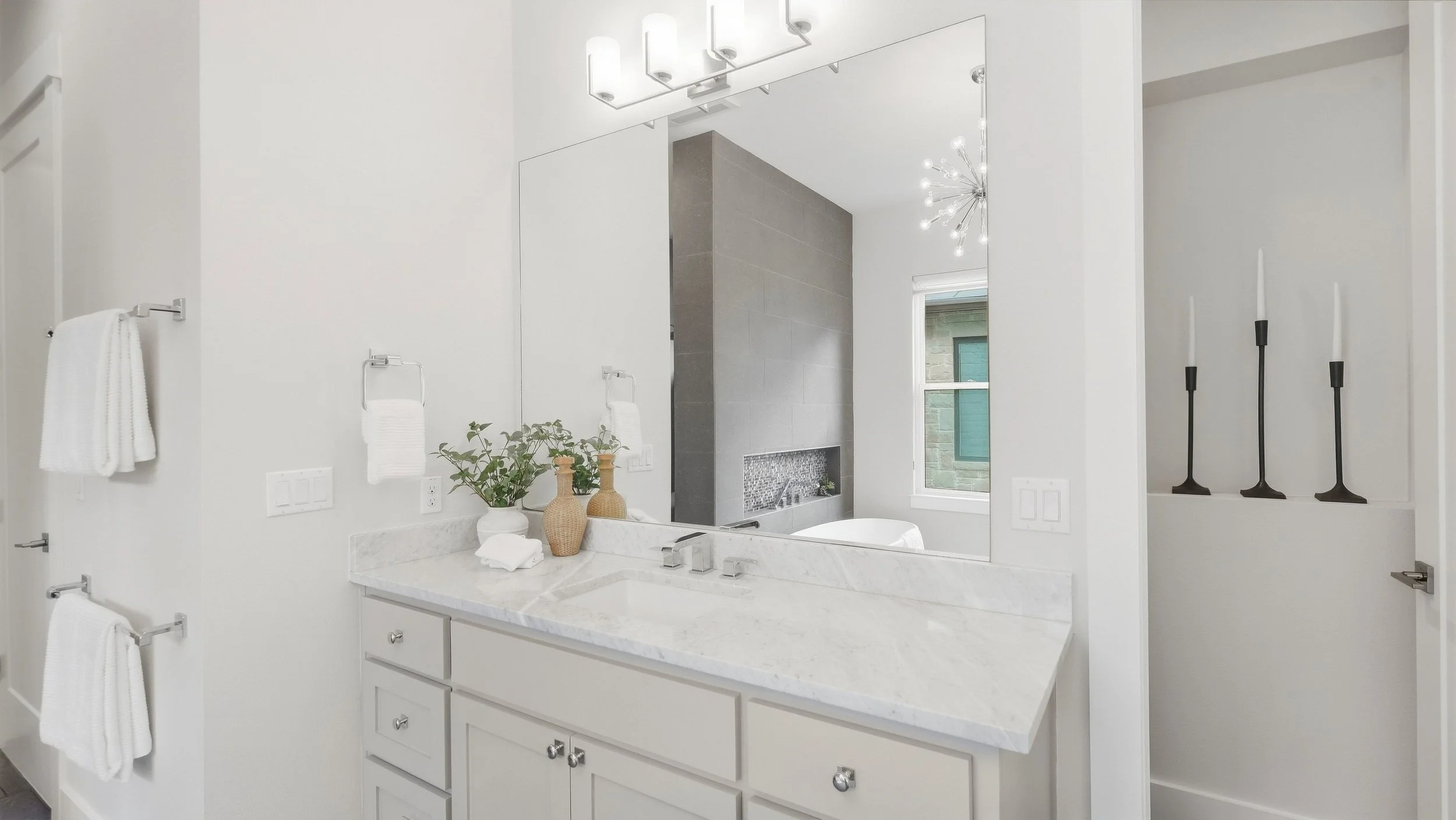 Primary bathroom vanity staged with woven vases, greenery, and black candlesticks beside a marble countertop.