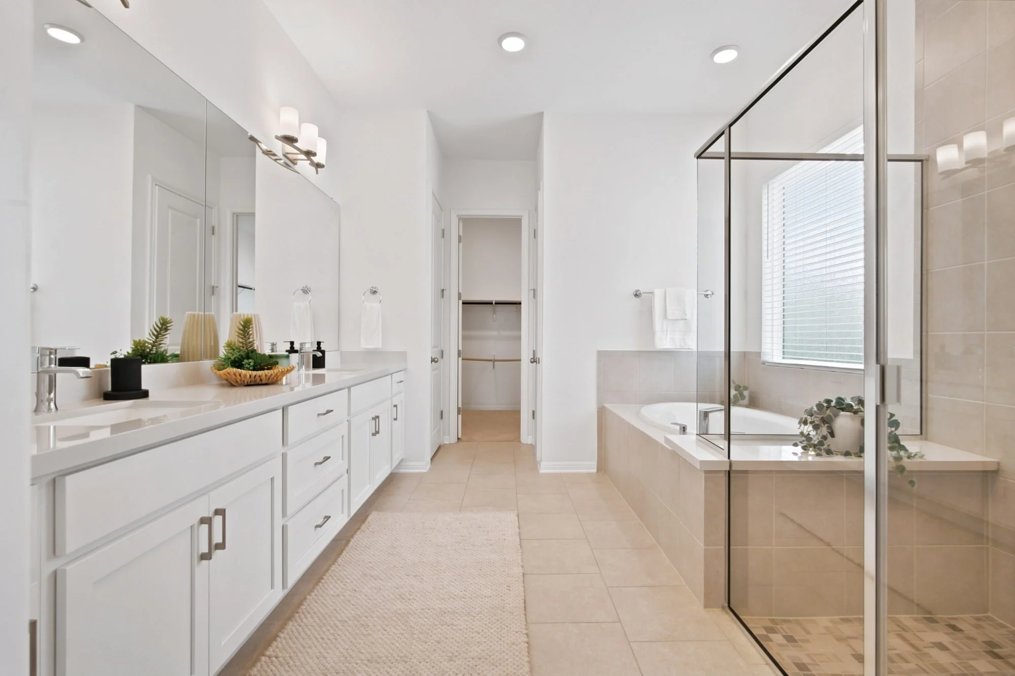 A long double vanity leads past a soaking tub toward the glass-enclosed shower.