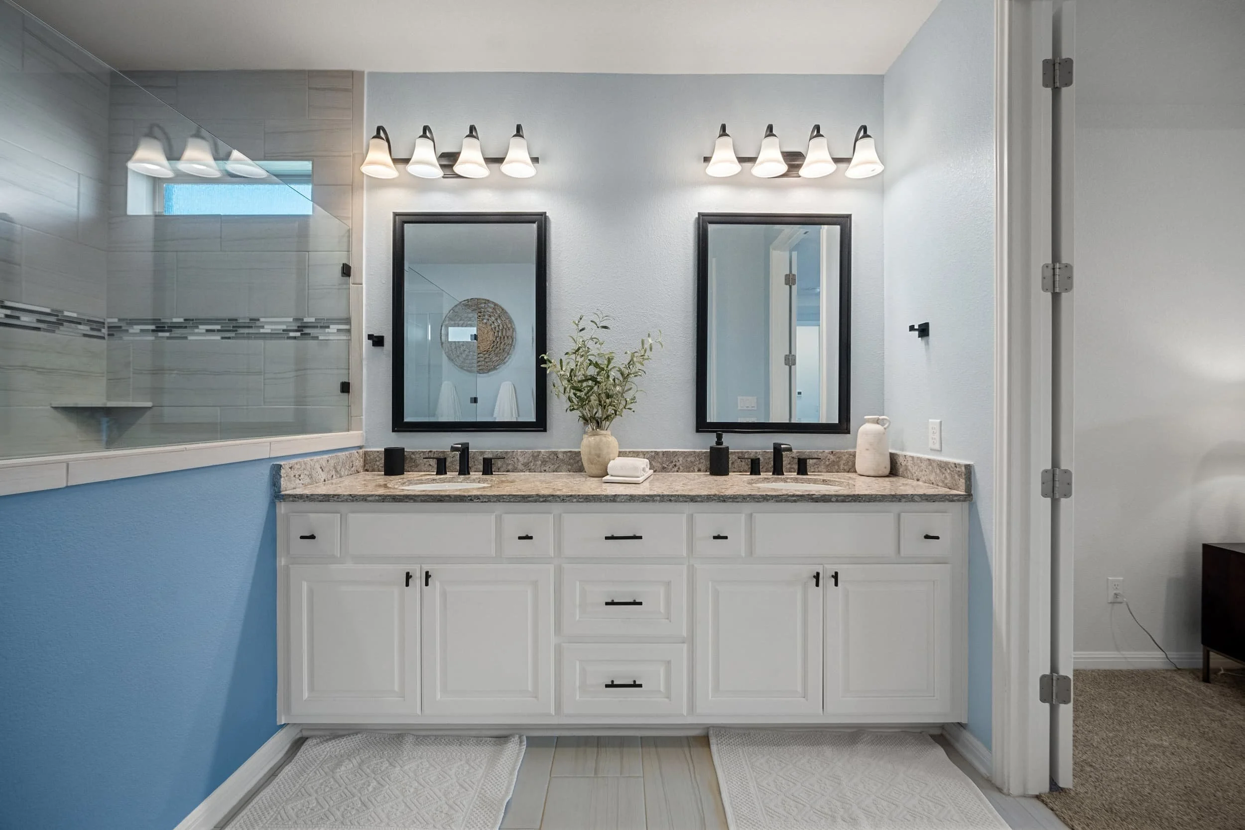 Staged Austin bathroom with light blue walls, granite countertops, black mirrors, and matte black fixtures.