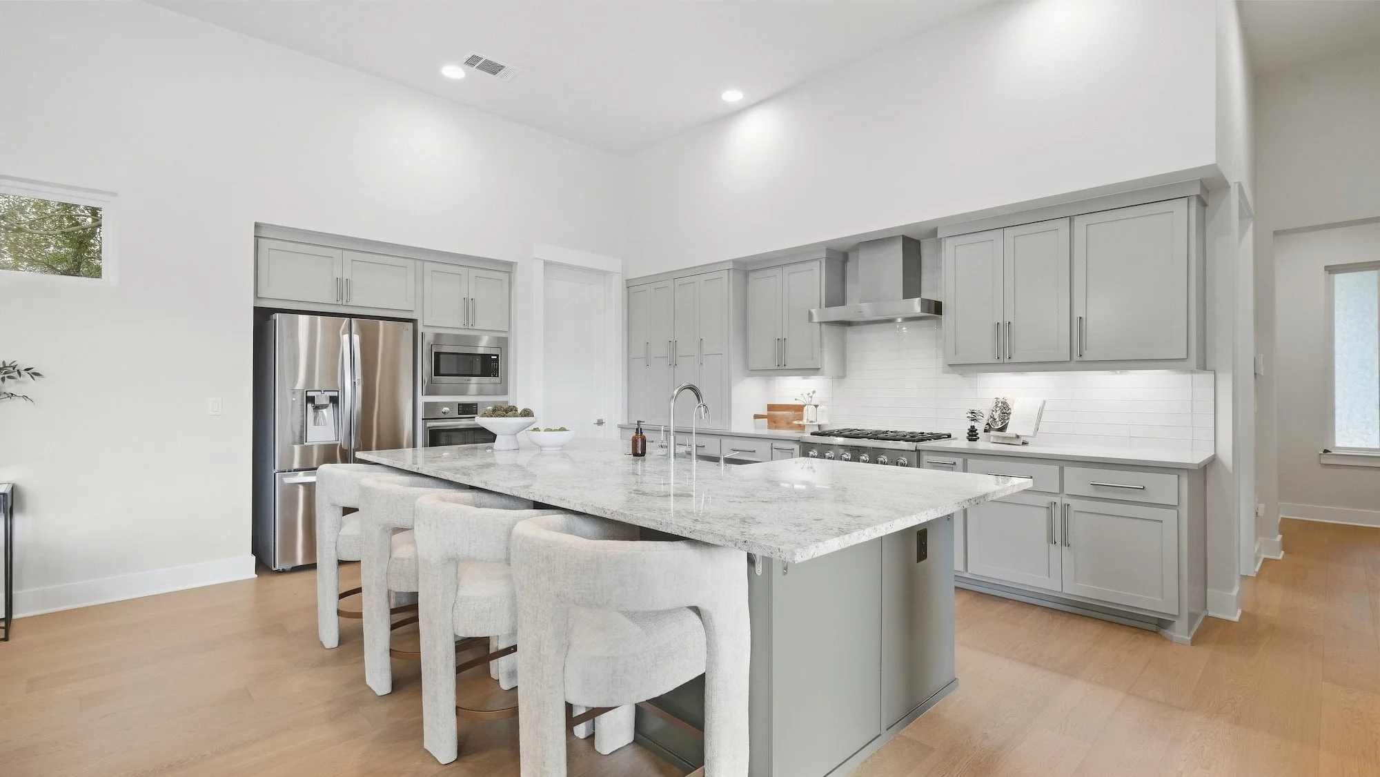Kitchen staged with four upholstered counter stools at a granite island and gray shaker cabinets.