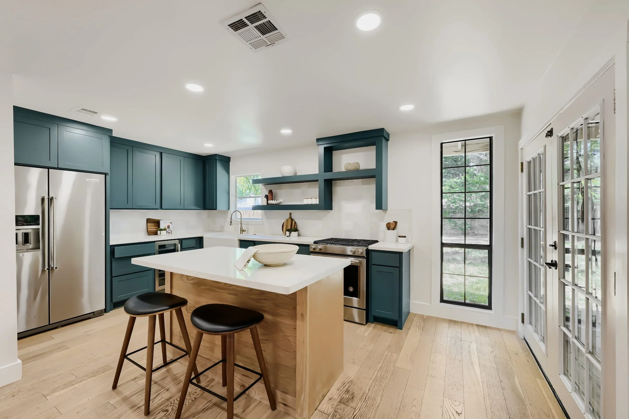 Staged kitchen with teal cabinets and a wood island, opening through glass french doors to the backyard.