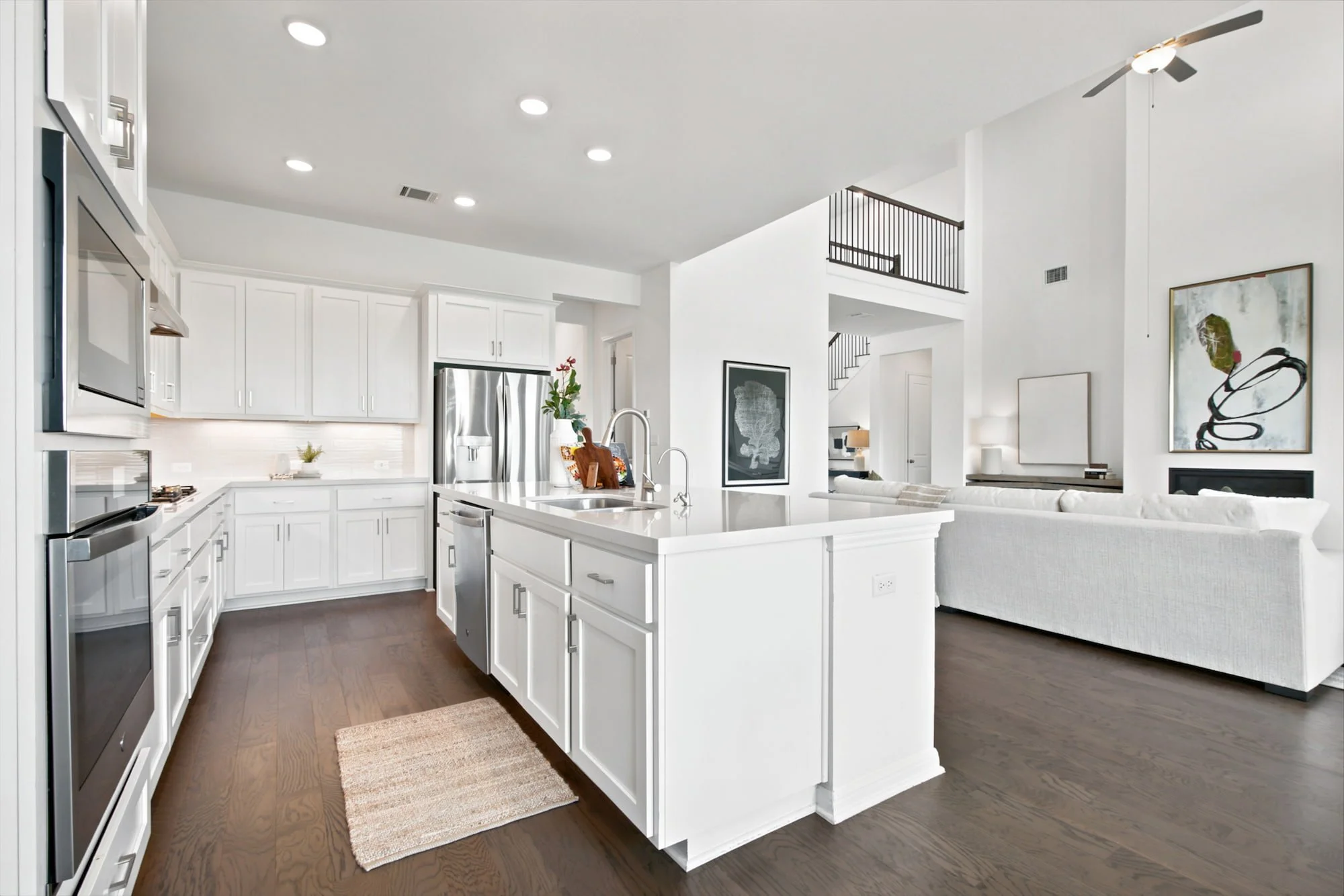 A white kitchen island flows into a sunlit living room beneath a two-story open railing.