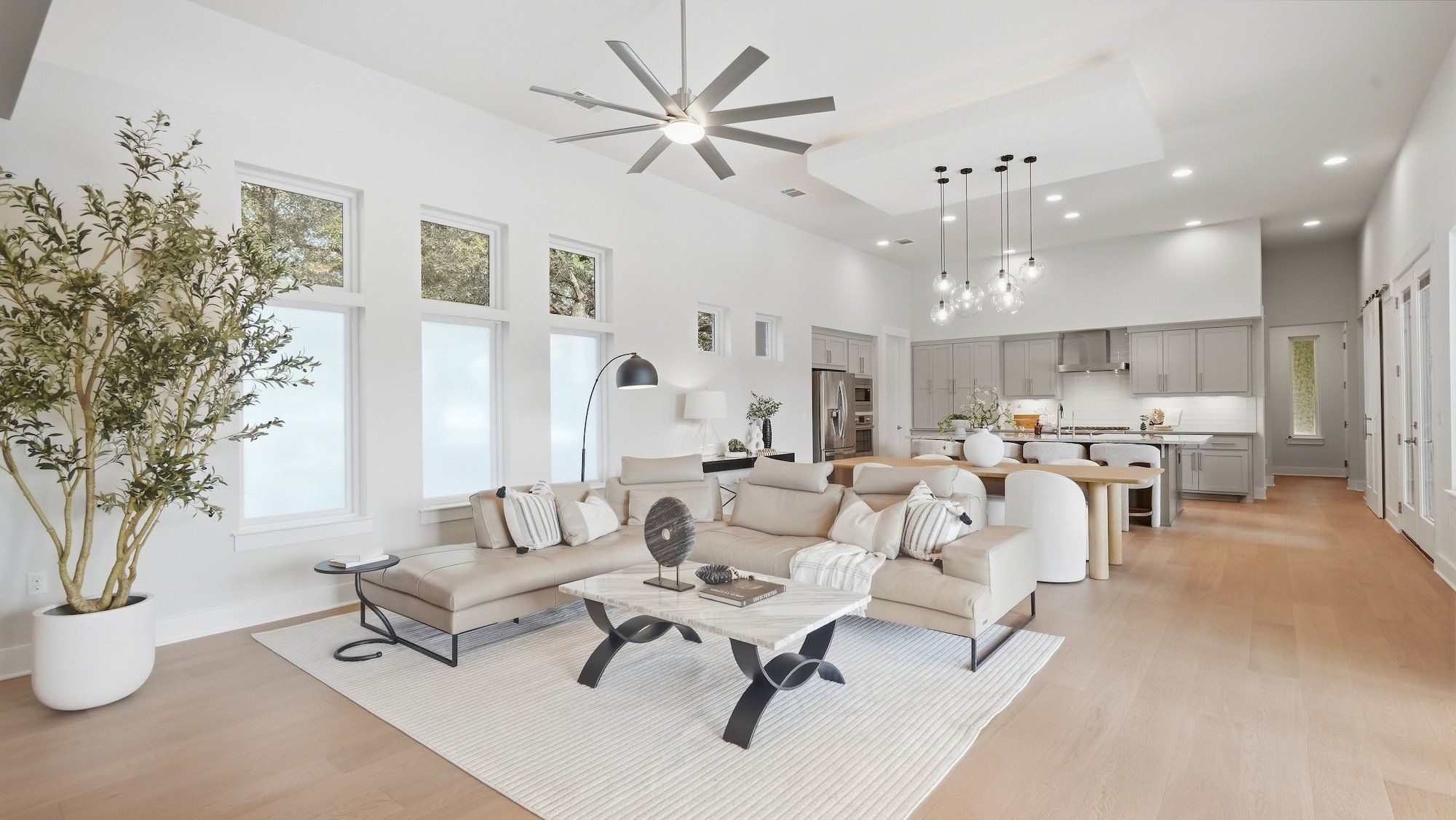 Open living, dining, and kitchen space staged with a cream sectional, marble coffee table, and globe pendants.