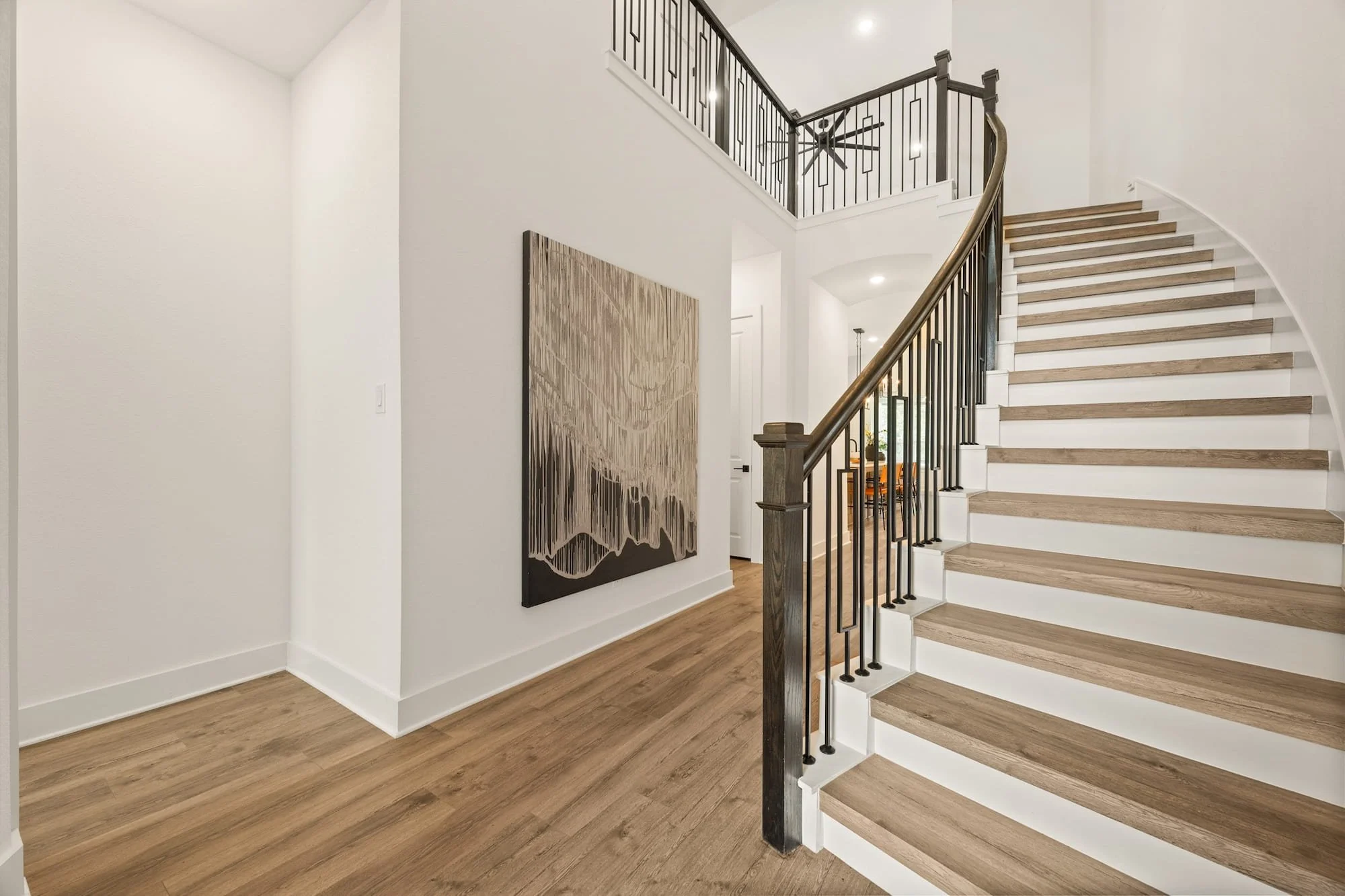 Grand entry staircase with custom iron balusters, soaring ceilings, and warm wood-look flooring