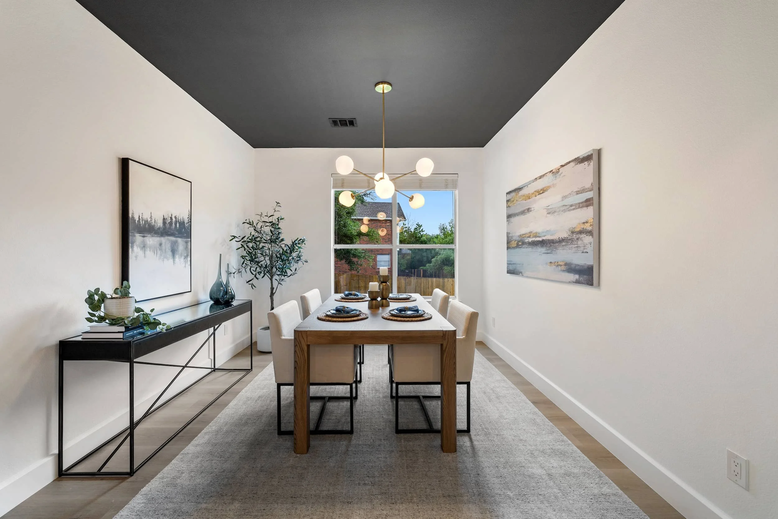 Elegant dining room with wood table, upholstered chairs, statement chandelier, dark accent ceiling, and large window.