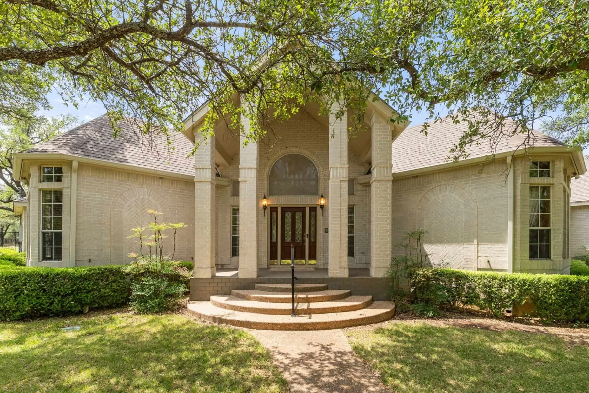 Front exterior of a two-story brick home in Georgetown with a covered entrance, white columns, and mature oak trees.
