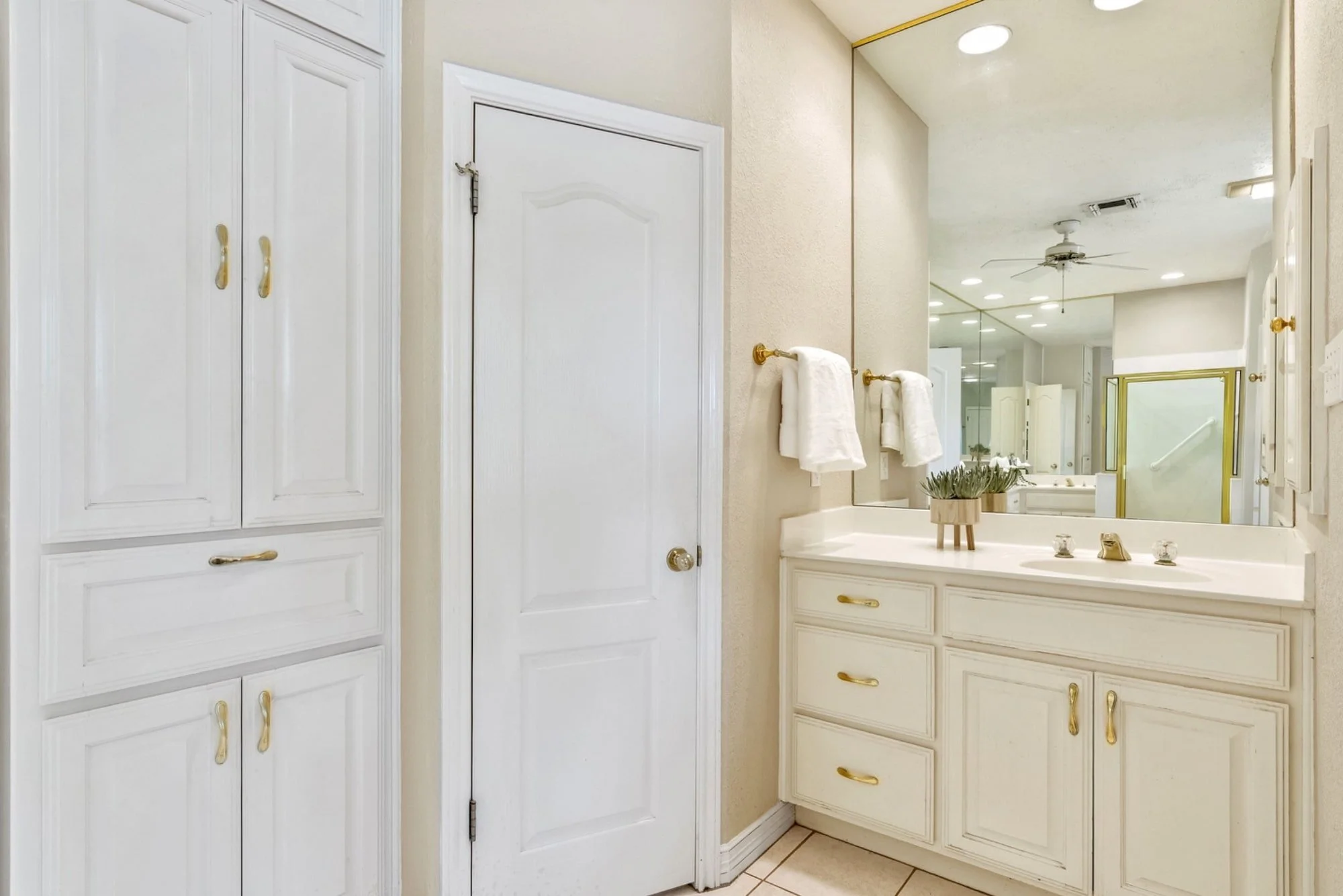 Primary bathroom vanity with built-in storage, gold-tone fixtures, and a large wall mirror.