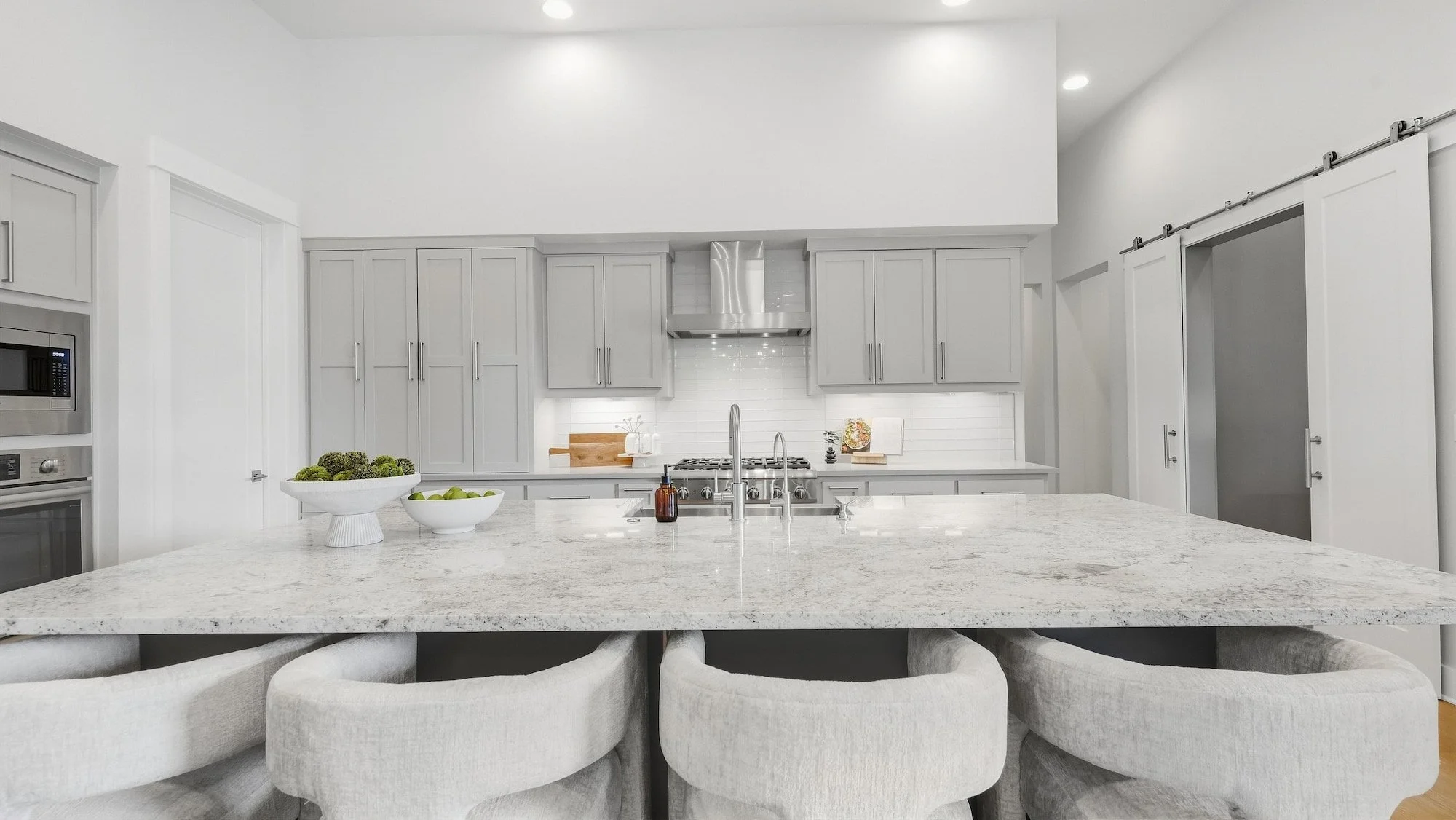 Kitchen staged with a granite island, white fruit bowls, and sliding barn doors to the side.