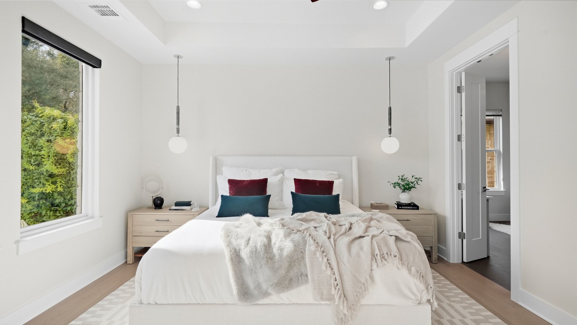 Primary bedroom staged with a white upholstered bed, jewel-tone velvet pillows, and matching globe pendants.
