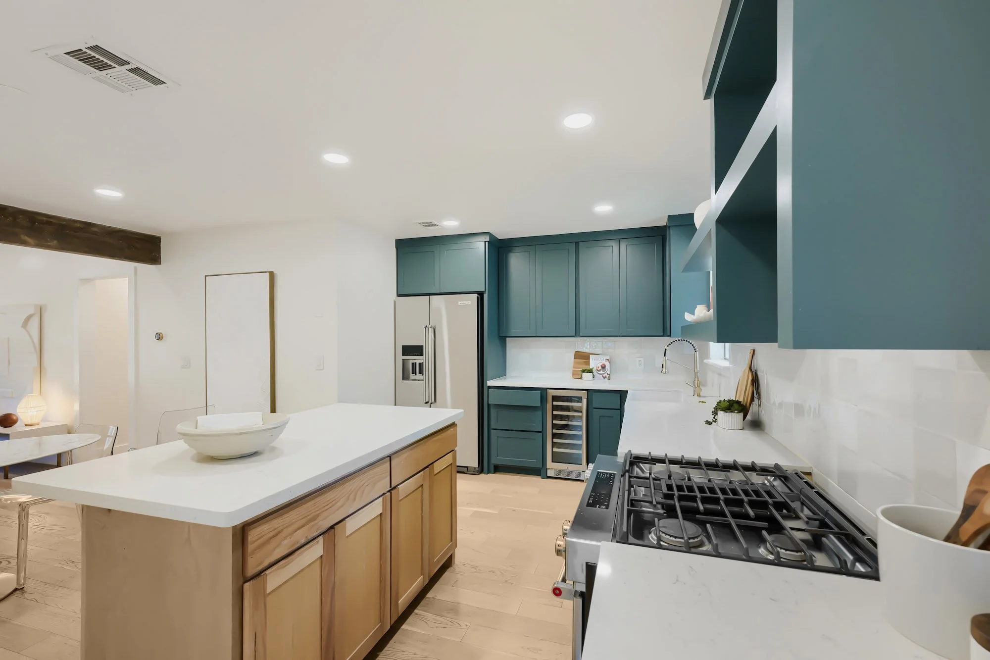 Staged kitchen with teal shaker cabinets, a stainless gas range, and a light wood island topped in white quartz.