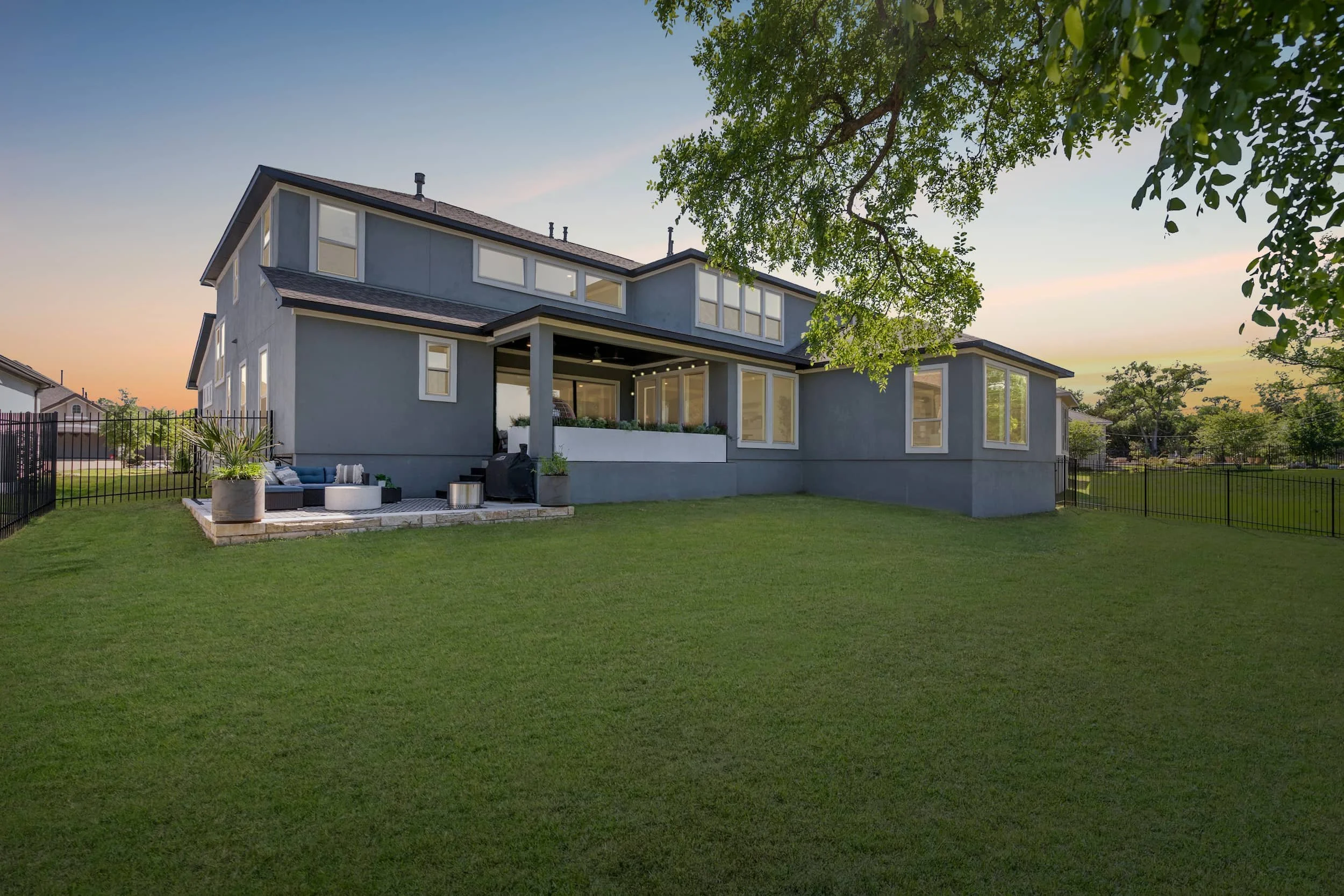 Modern backyard with spacious covered patio, outdoor seating, fire pit, and expansive green lawn.