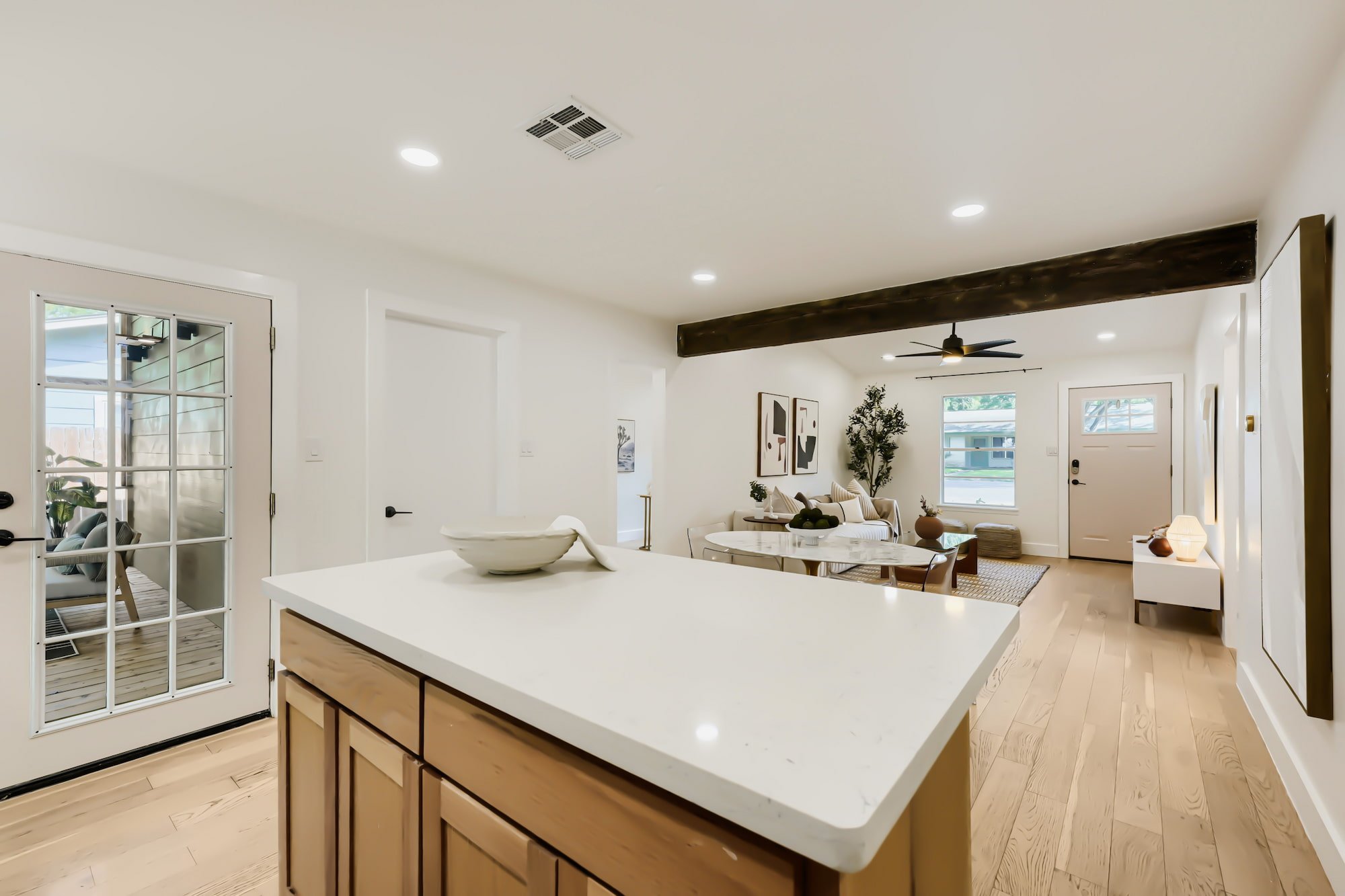Staged kitchen island in white quartz and light wood, looking across an open plan to the dining table and living room beyond.