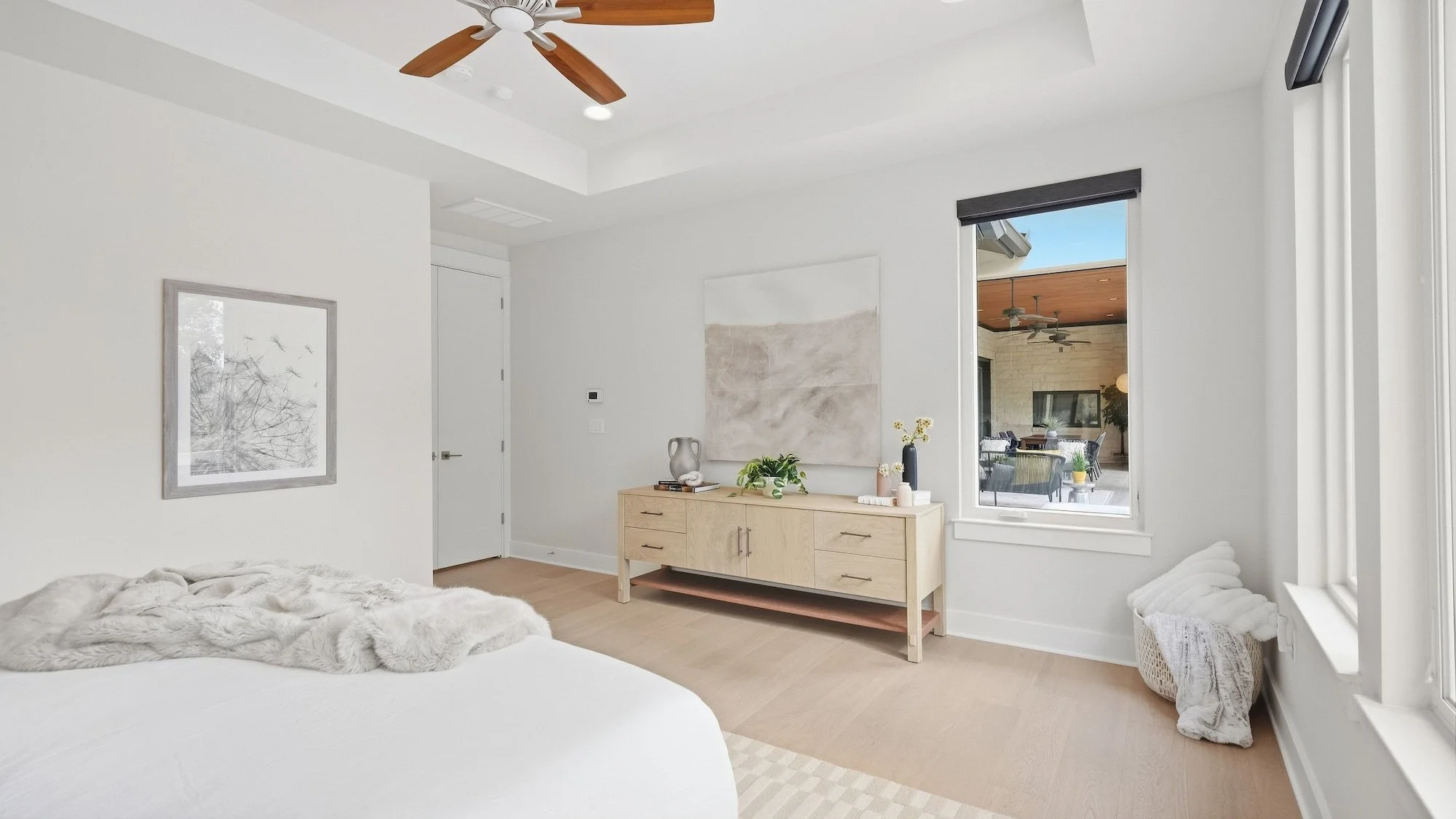 Primary bedroom staged with a light oak dresser, neutral abstract art, and a window to the covered patio.