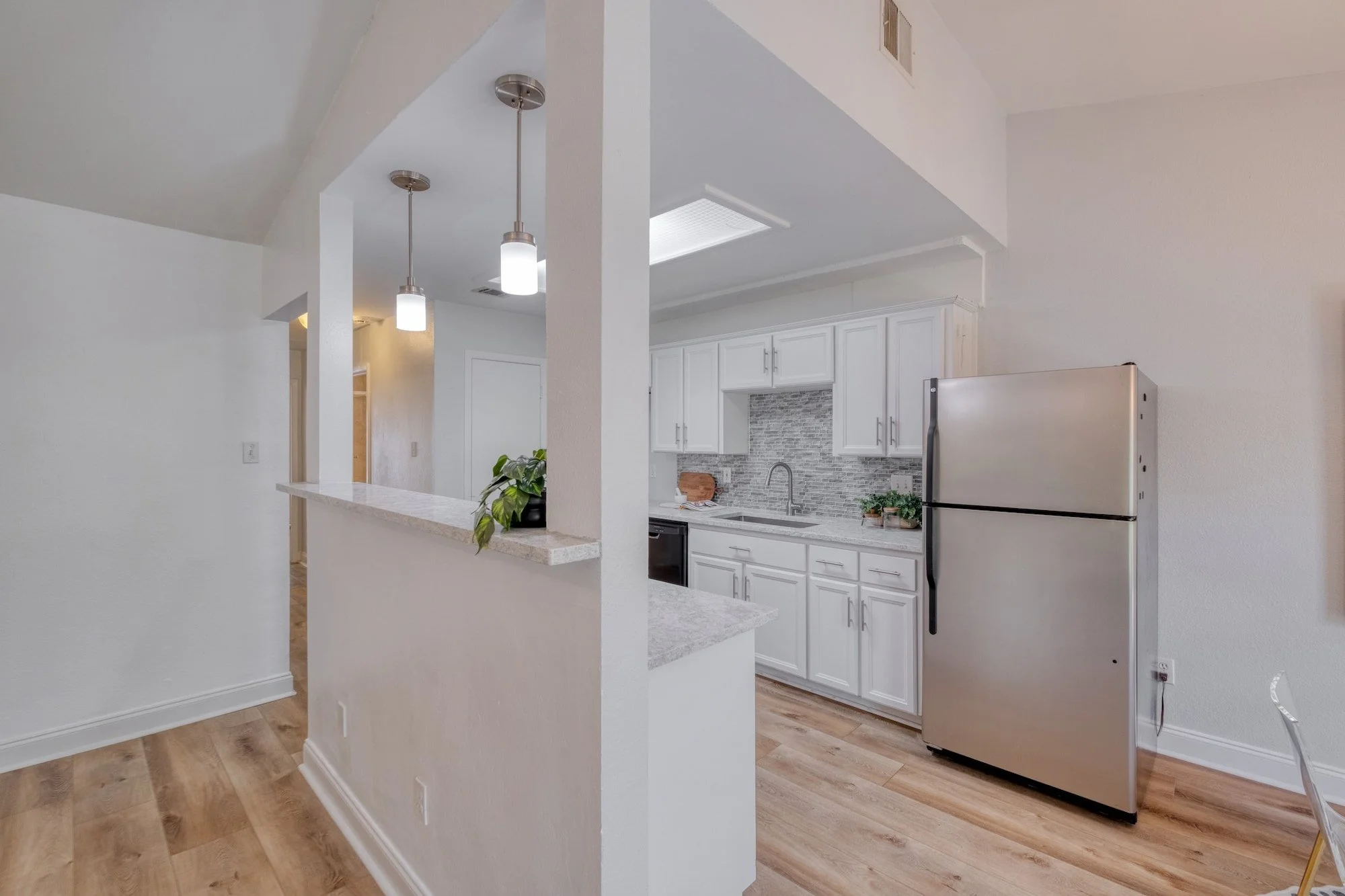 Bright white kitchen with breakfast bar, pendant lighting, stainless steel appliances, and modern finishes.