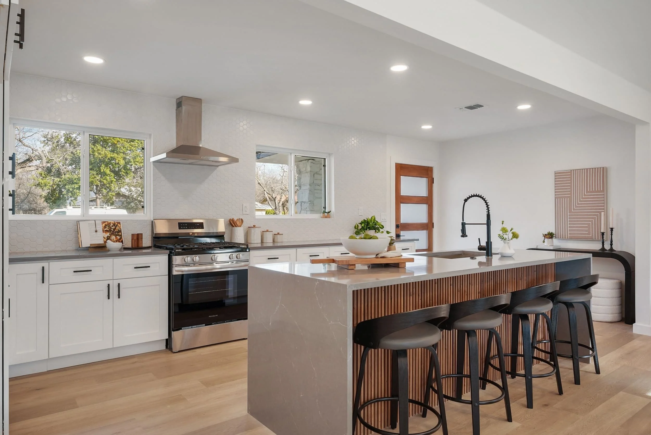 Modern kitchen with large island and bar seating, white cabinets, stainless steel range, tile backsplash, and natural light.