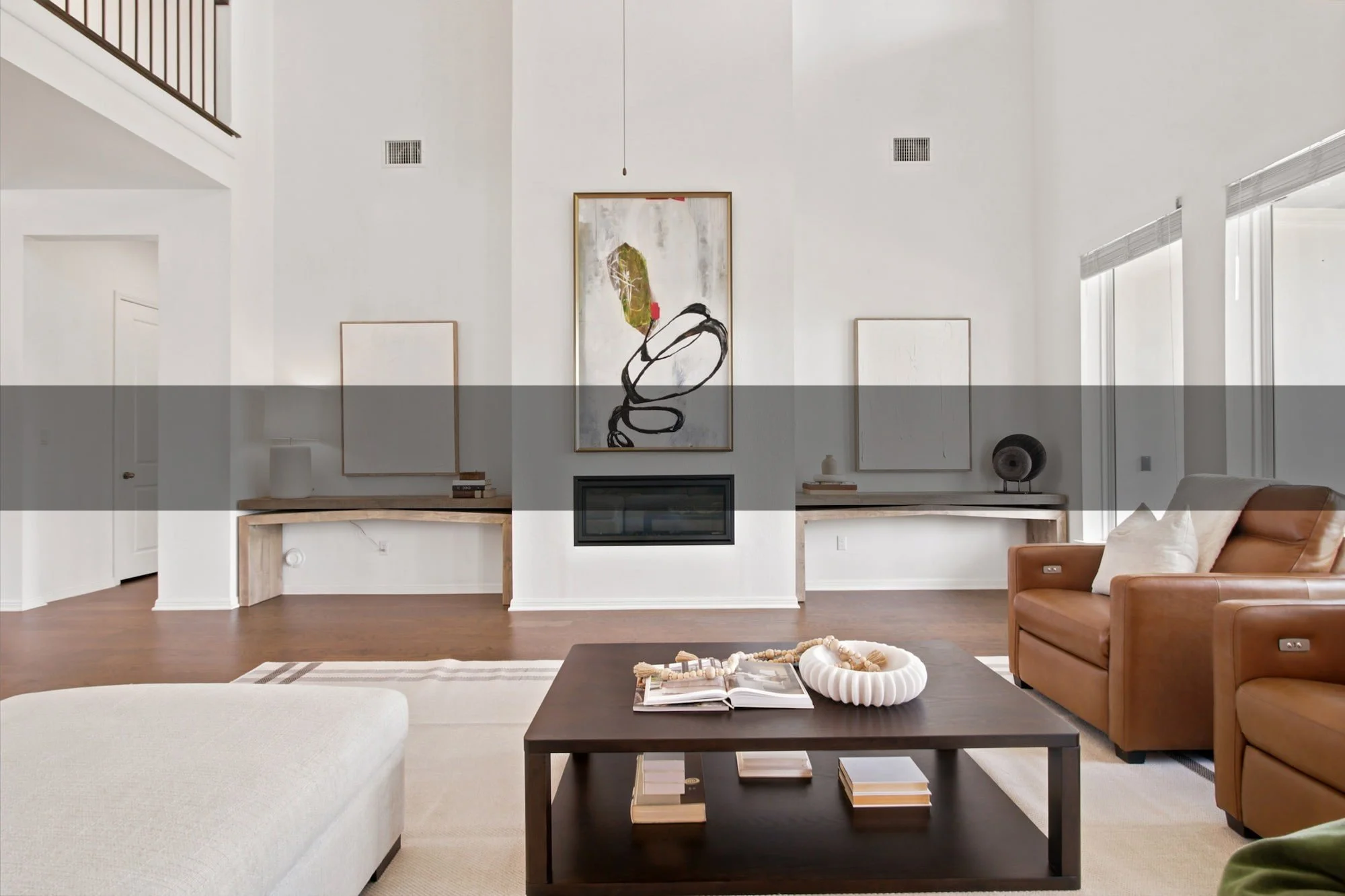 Layered art and a fireplace anchor the two-story living room's main wall.