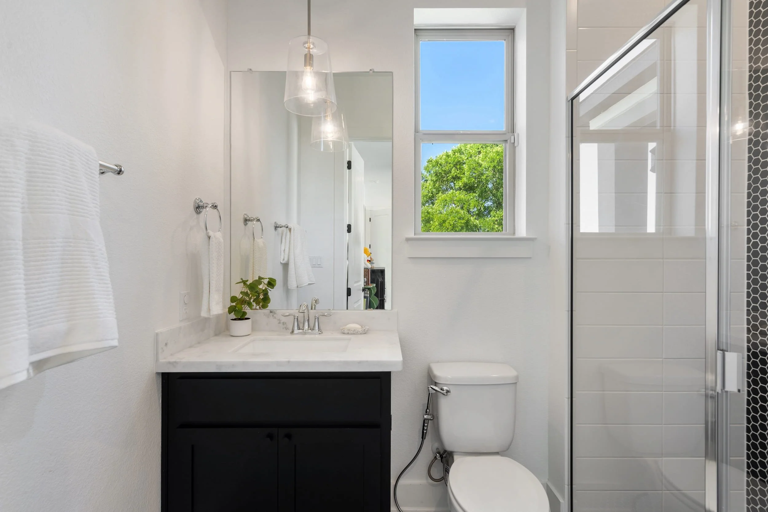 Bathroom with single vanity, marble countertop, glass shower, white tile, black cabinet, compact layout.