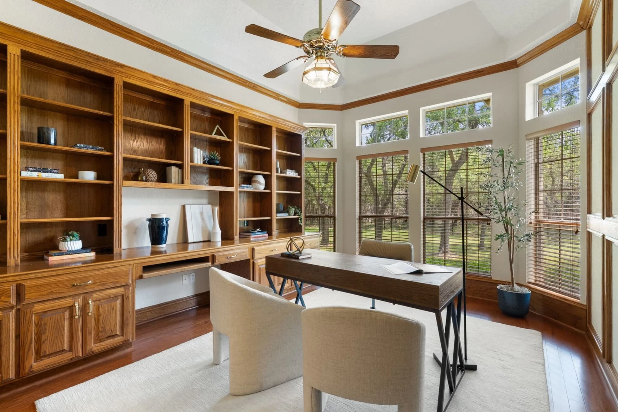 Home office with built-in bookshelves, a workspace, and large windows overlooking mature oak trees.