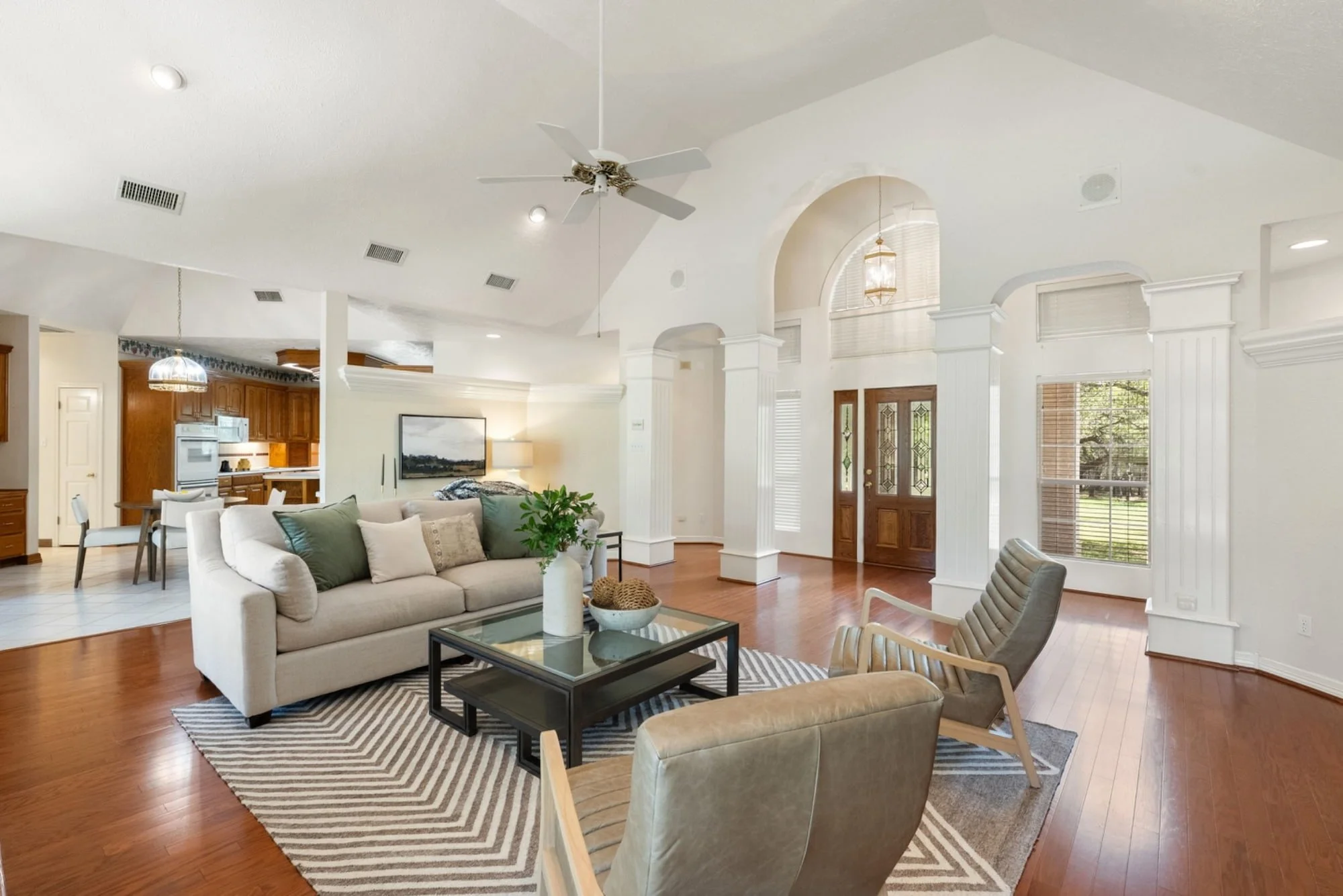 Open living area with vaulted ceilings, hardwood floors, and a view of the front entry and kitchen.