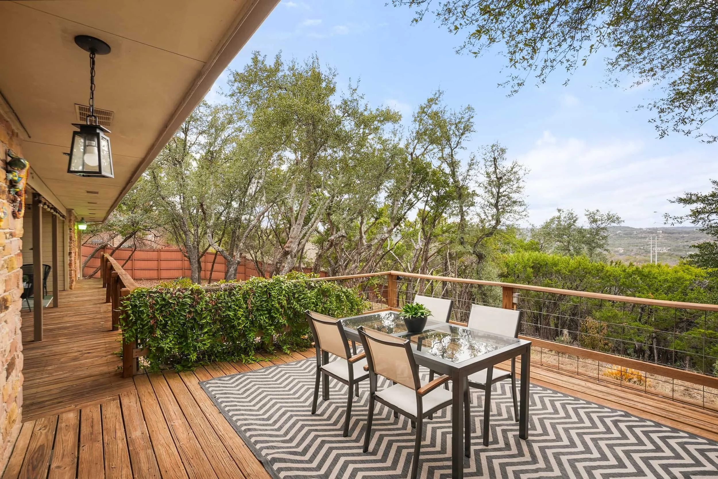 Covered deck with outdoor dining table, wood railing, and scenic views of trees and surrounding hills.