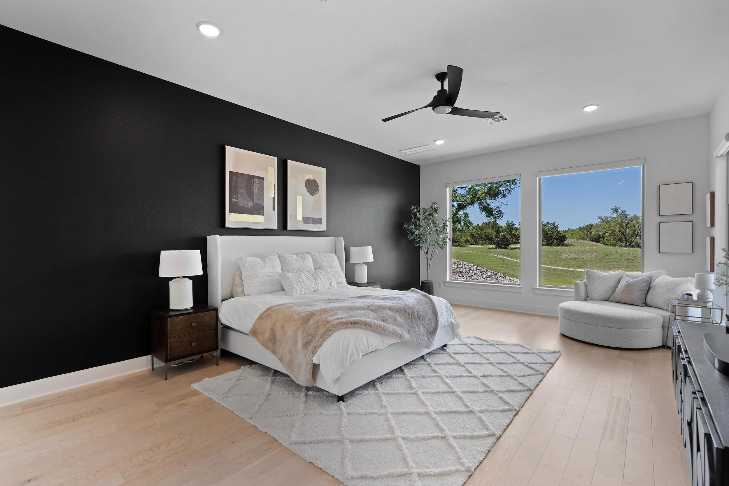 Elegantly staged bedroom with black accent wall, upholstered bed, large windows, neutral decor.