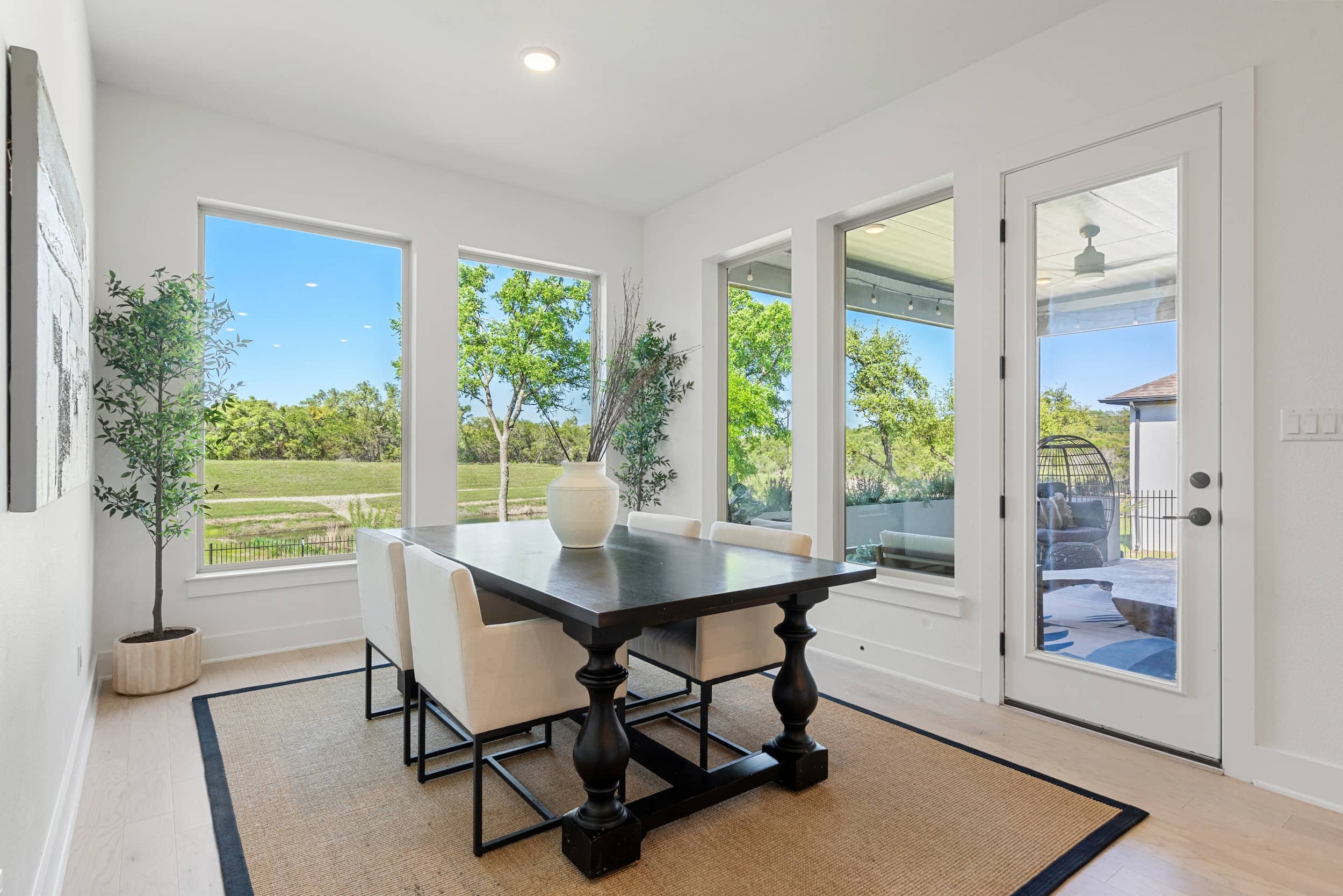 Dining room staging with black table, upholstered chairs, large windows, nature views, indoor outdoor connection.