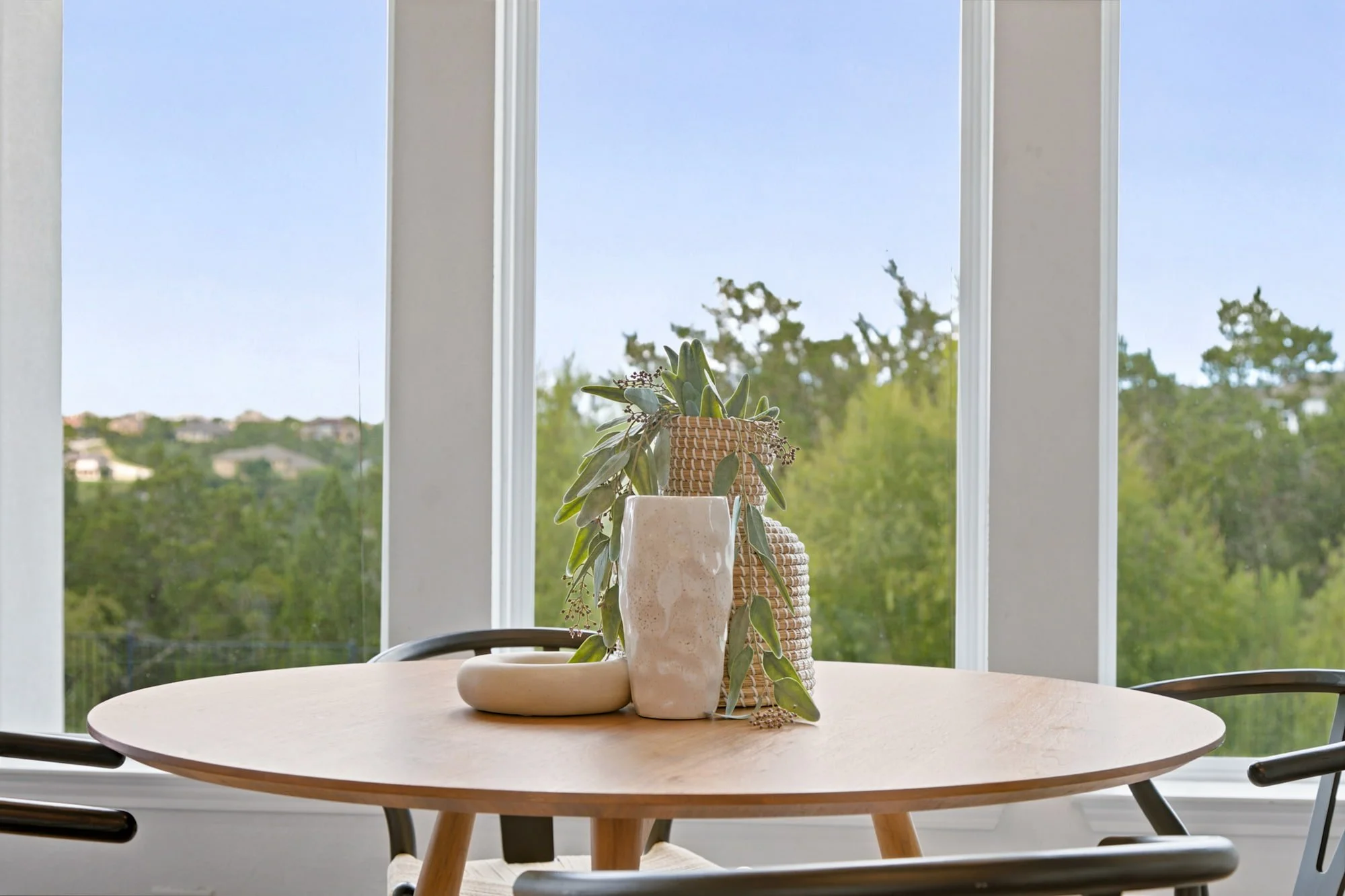 Ceramic vases and greenery style the breakfast table against a wall of tree-lined windows.