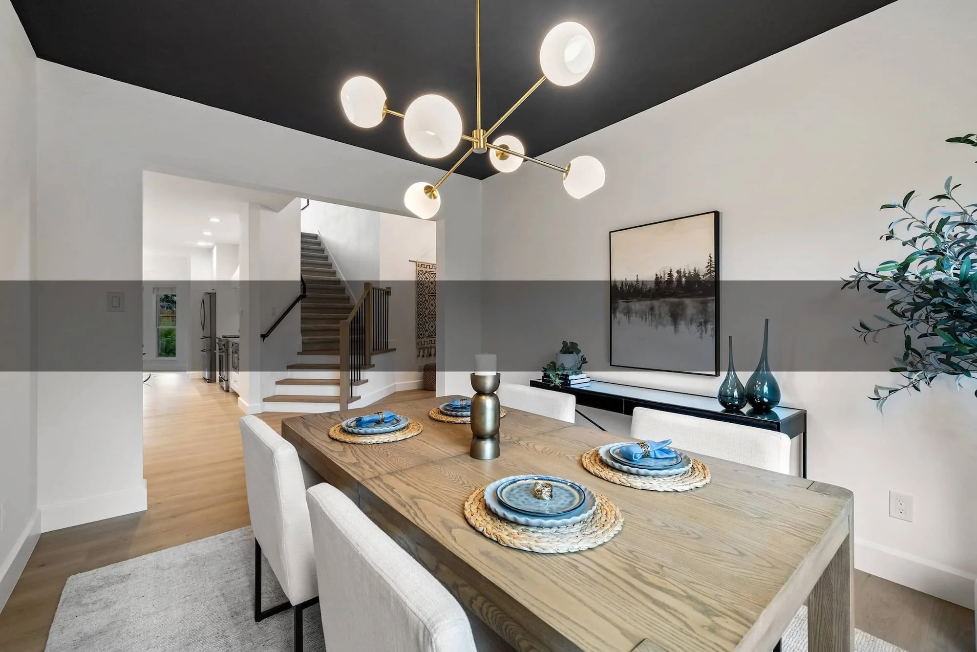Professionally staged dining room featuring a black statement ceiling, globe chandelier, and light wood table with blue accents.
