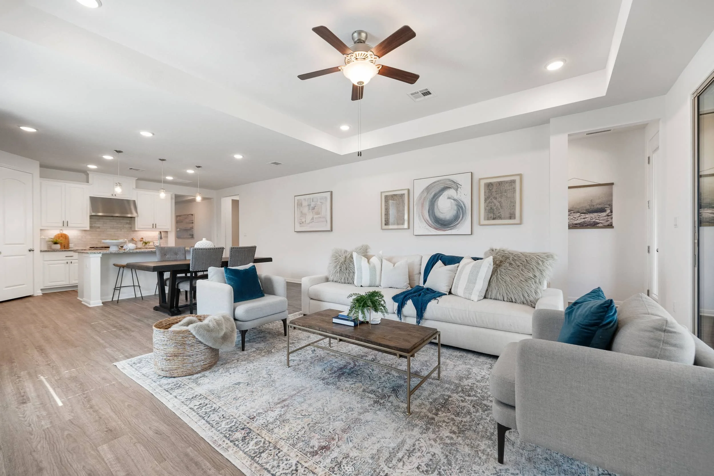 Airy open-plan living room in Austin with a tray ceiling and teal decor, featuring a dining area and white kitchen in the background.