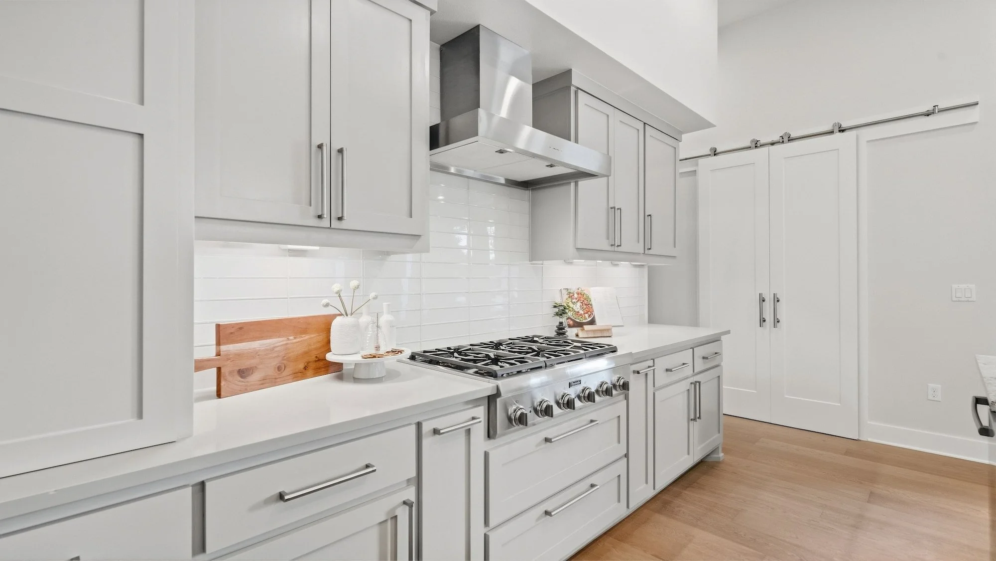 Kitchen range wall staged with a wood cutting board, white vases, and a cookbook on display.