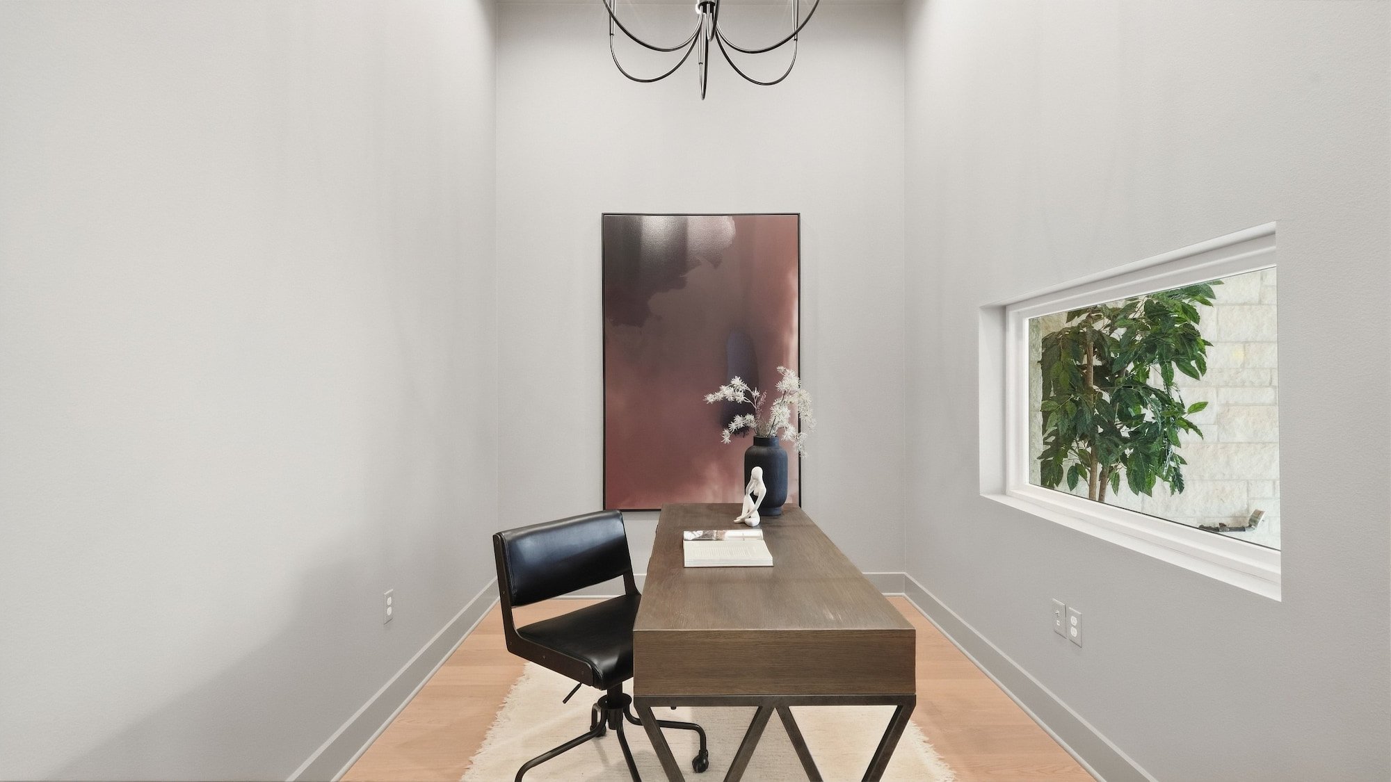 Home office staged with a wood desk, black leather chair, and a large abstract canvas.