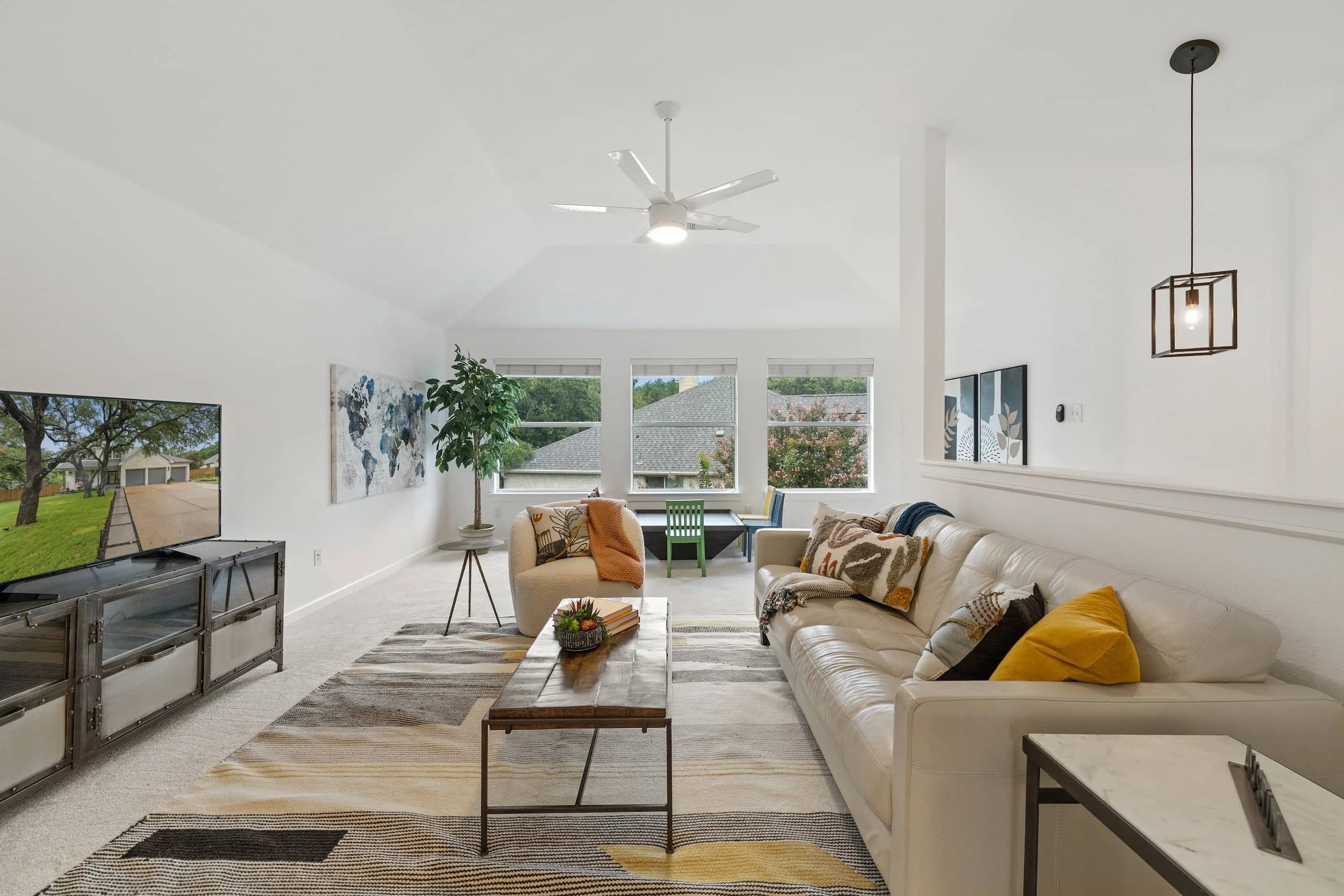 Bright family room with vaulted ceiling, beige sofa and chair, wood coffee table, TV console, and large windows for natural light.