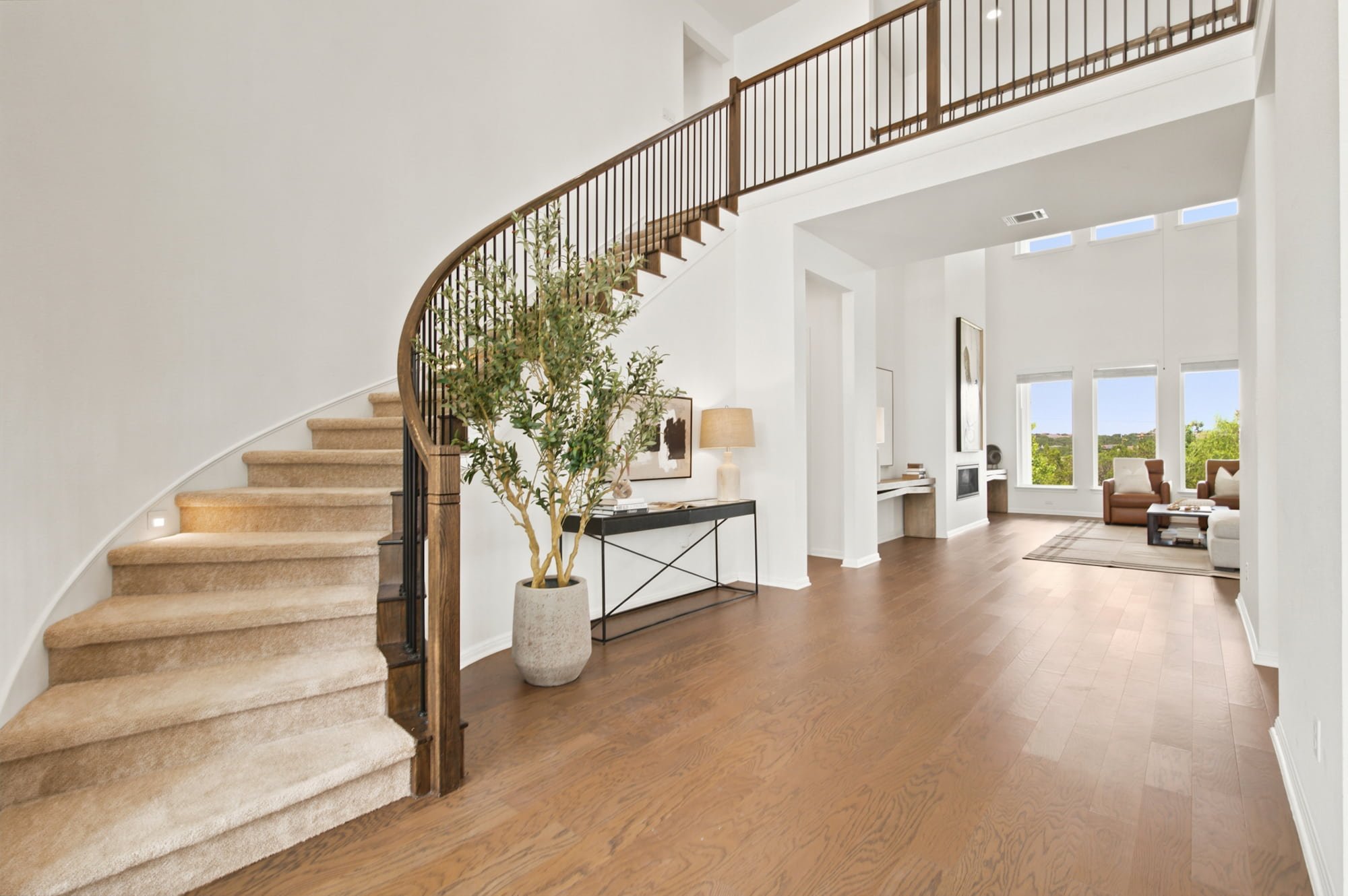 The curved staircase opens into a sunlit living room framed by tall windows.