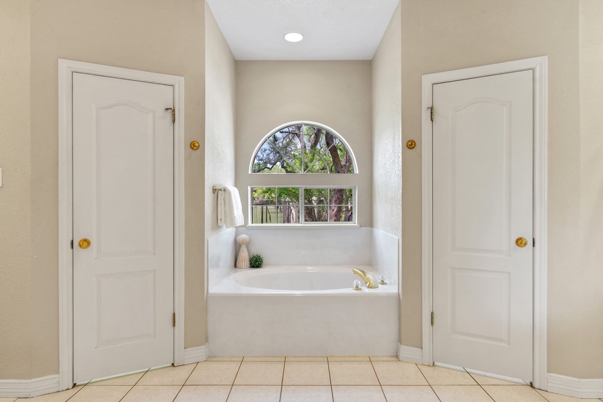 Primary bathroom soaking tub beneath an arched window with treetop views and abundant natural light.
