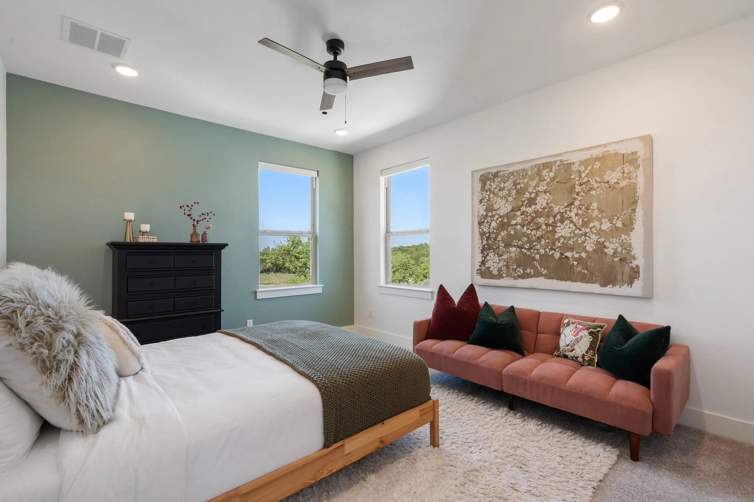 Modern staged guest bedroom featuring black dresser, neutral bedding, colorful pillows, and cozy seating area with shag rug.