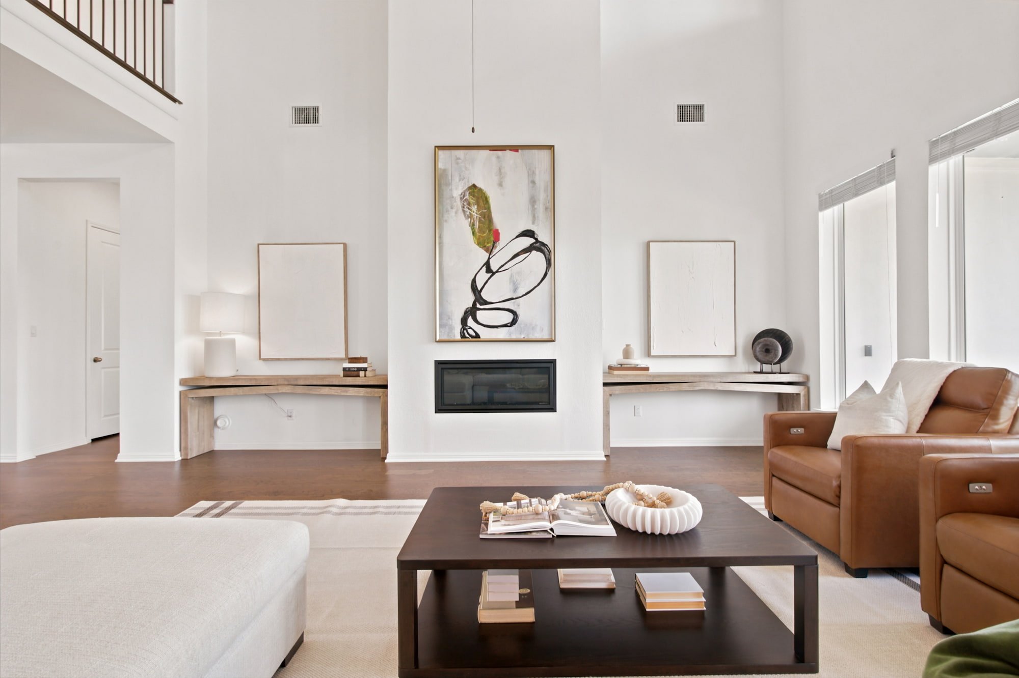 Layered art and a fireplace anchor the two-story living room's main wall.