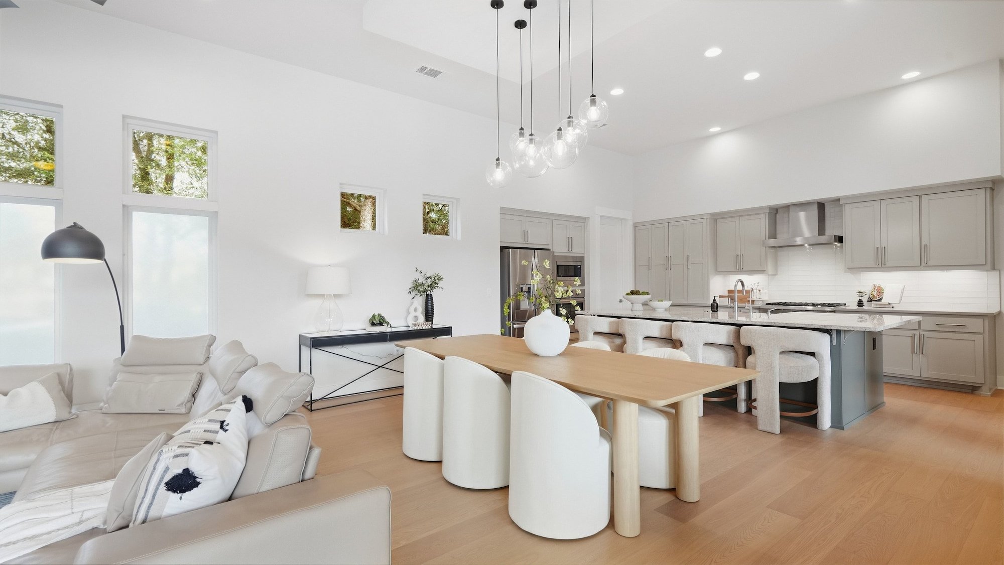 Open dining area staged with a light wood table, curved white chairs, and globe pendants near the kitchen.
