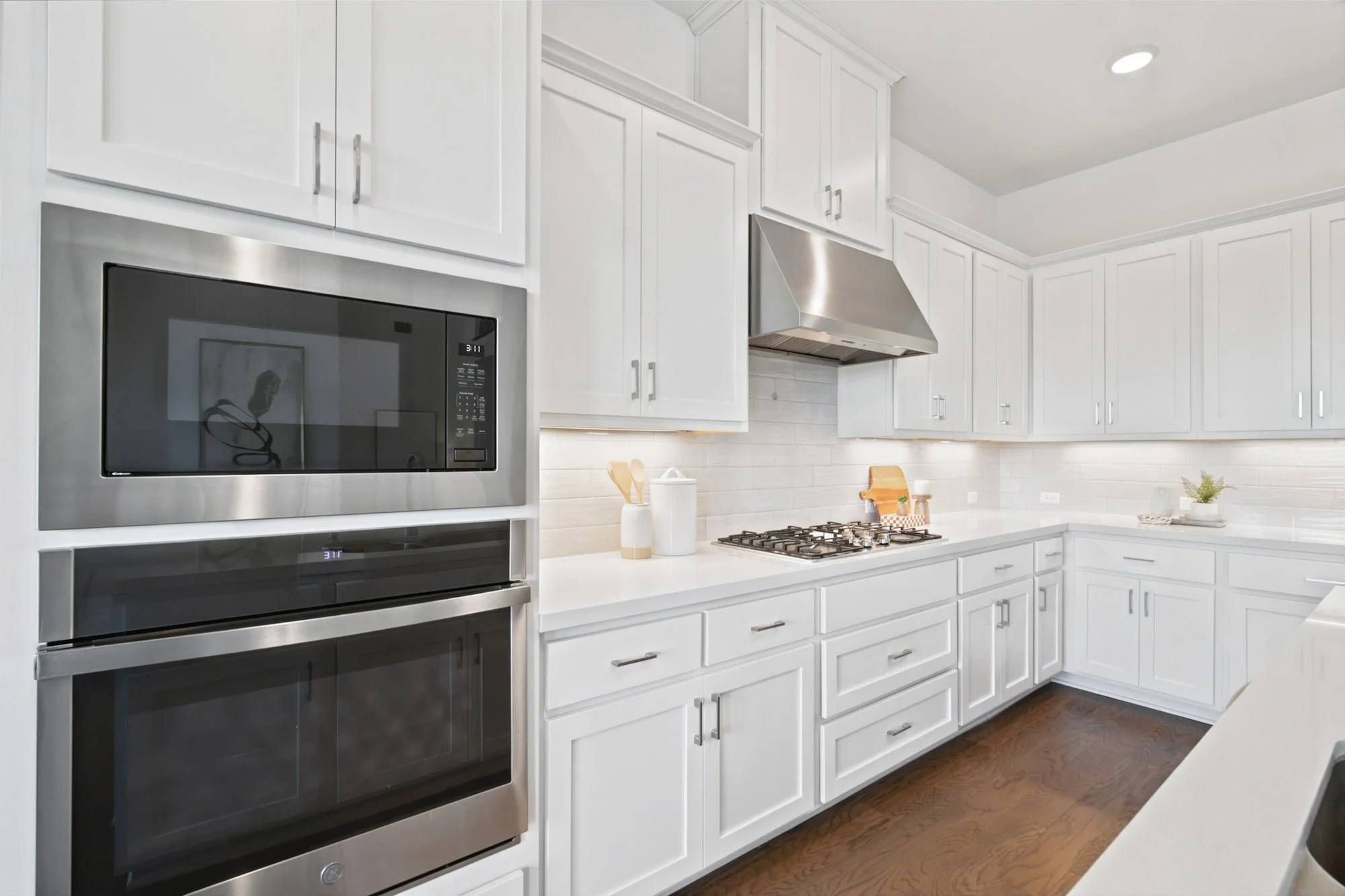 White cabinetry wraps the kitchen, with a gas cooktop styled with a cutting board and canister.