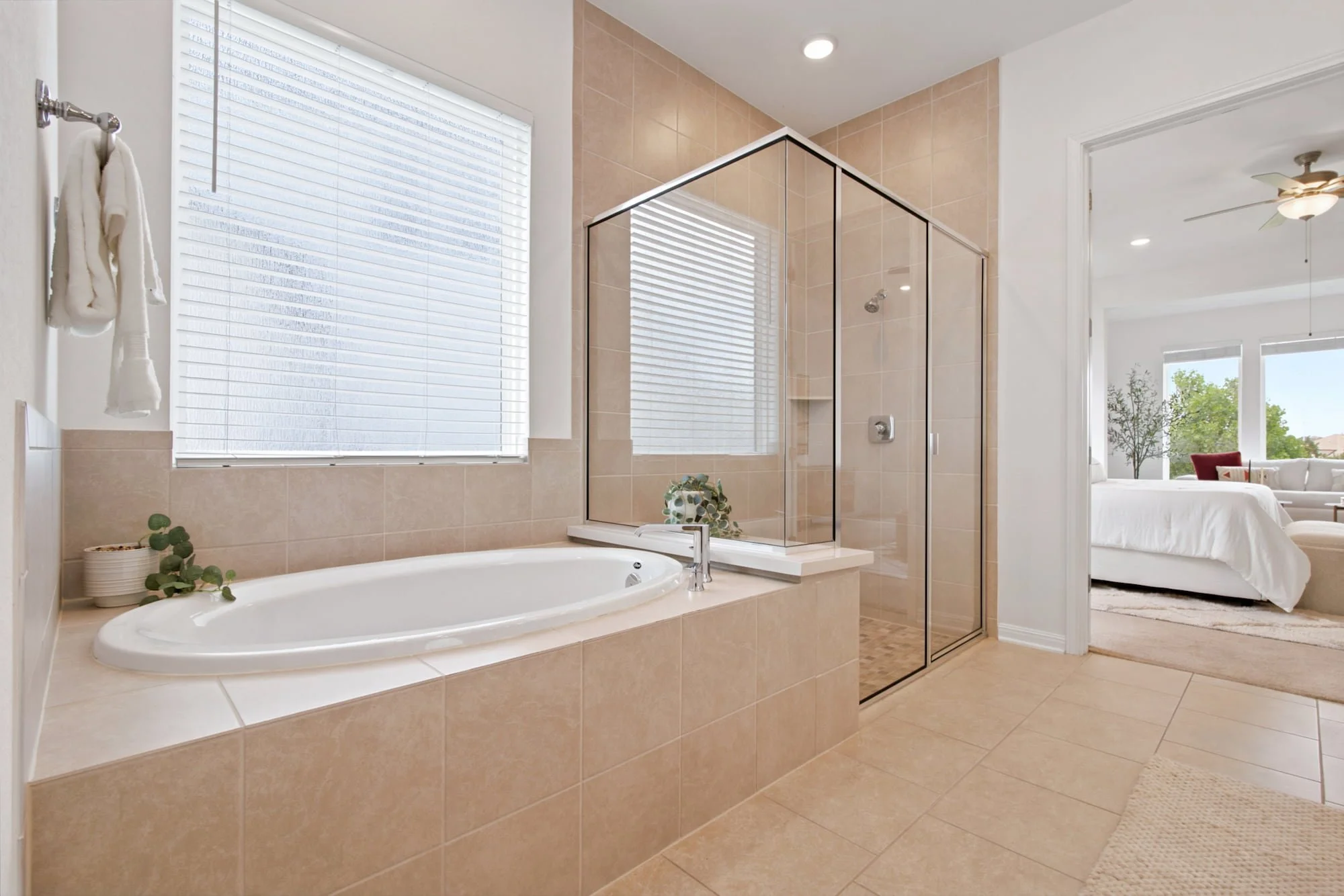 A soaking tub sits beside a glass shower, with the bedroom visible through the open door.