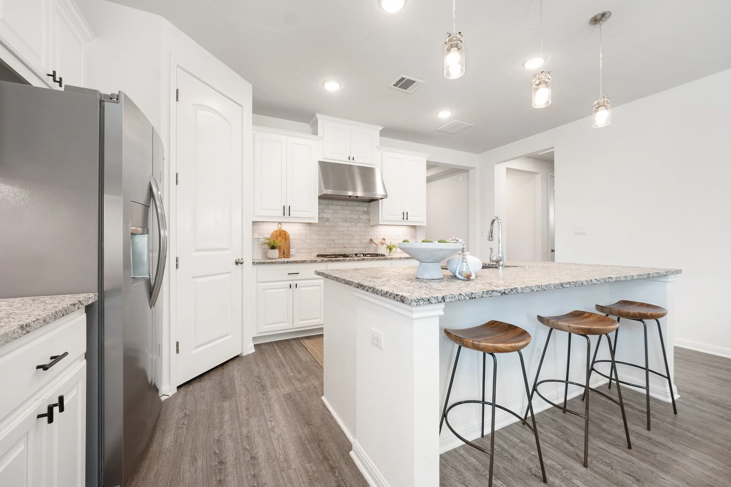 Expertly staged Austin kitchen featuring a large granite island, white shaker cabinets, and mid-century modern wood stools.