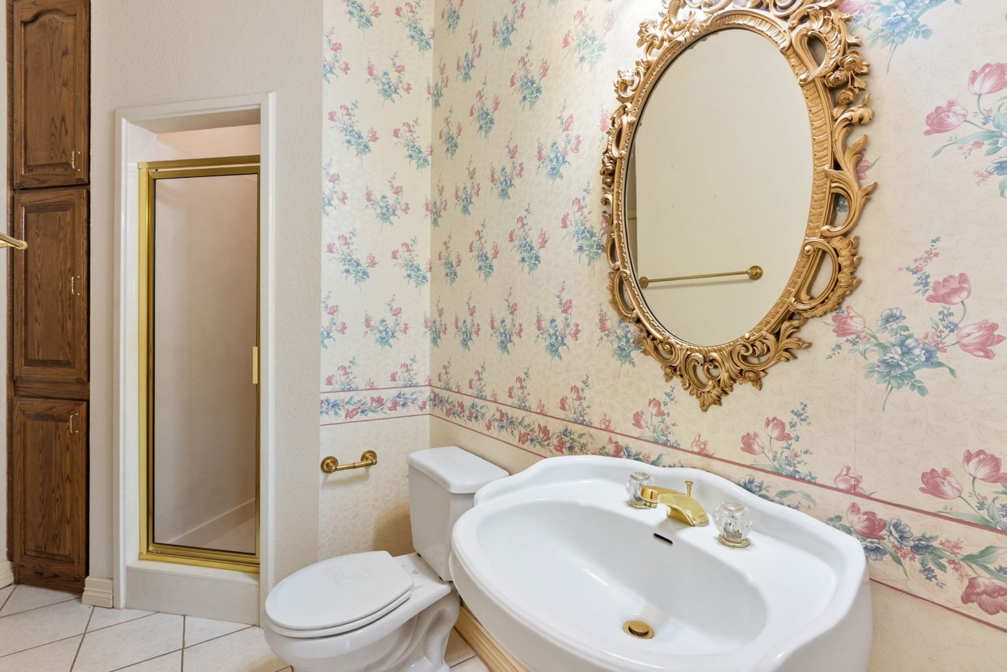 Powder bathroom with floral wallpaper, a decorative mirror, and gold-tone fixtures.