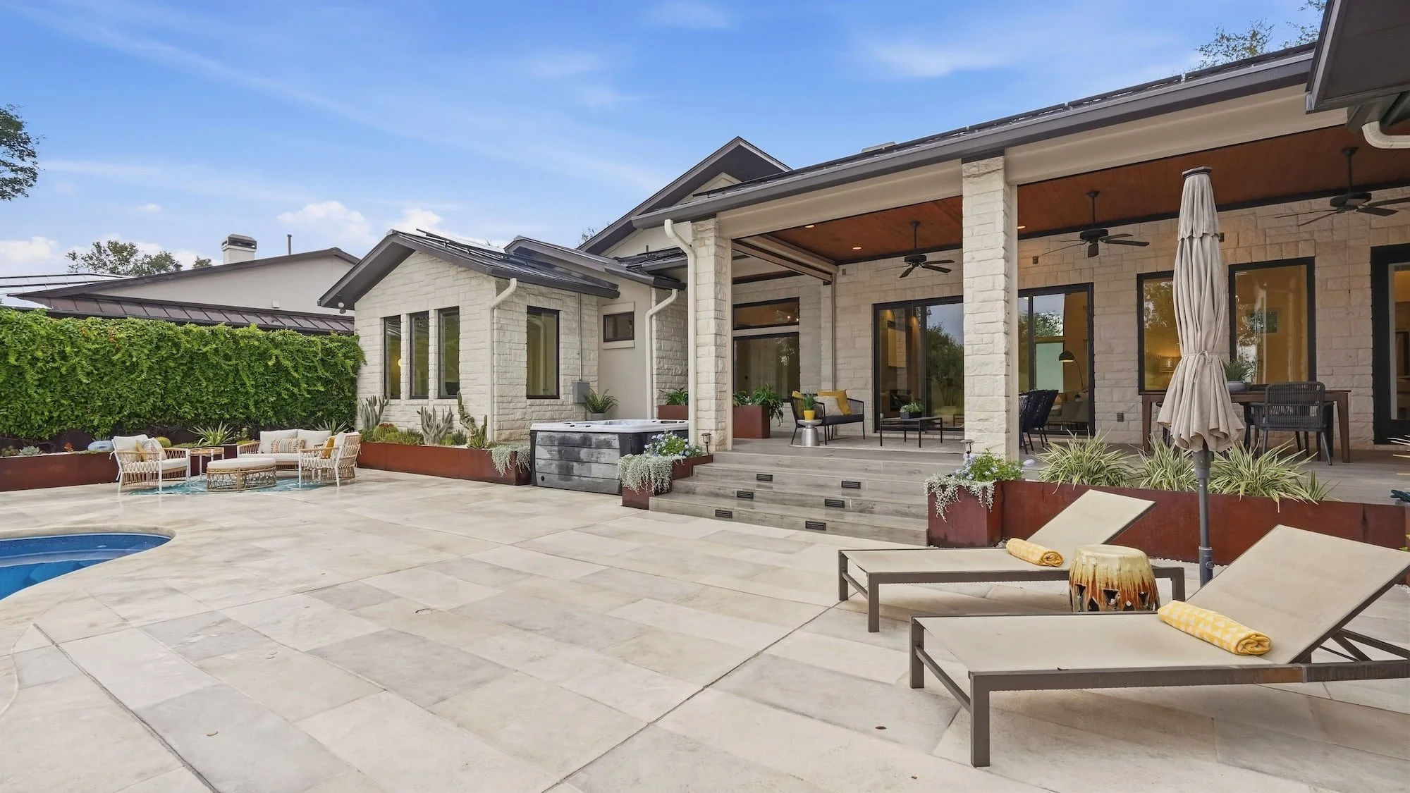 Pool deck staged with lounge chairs and yellow towels, plus wicker seating near the covered patio.