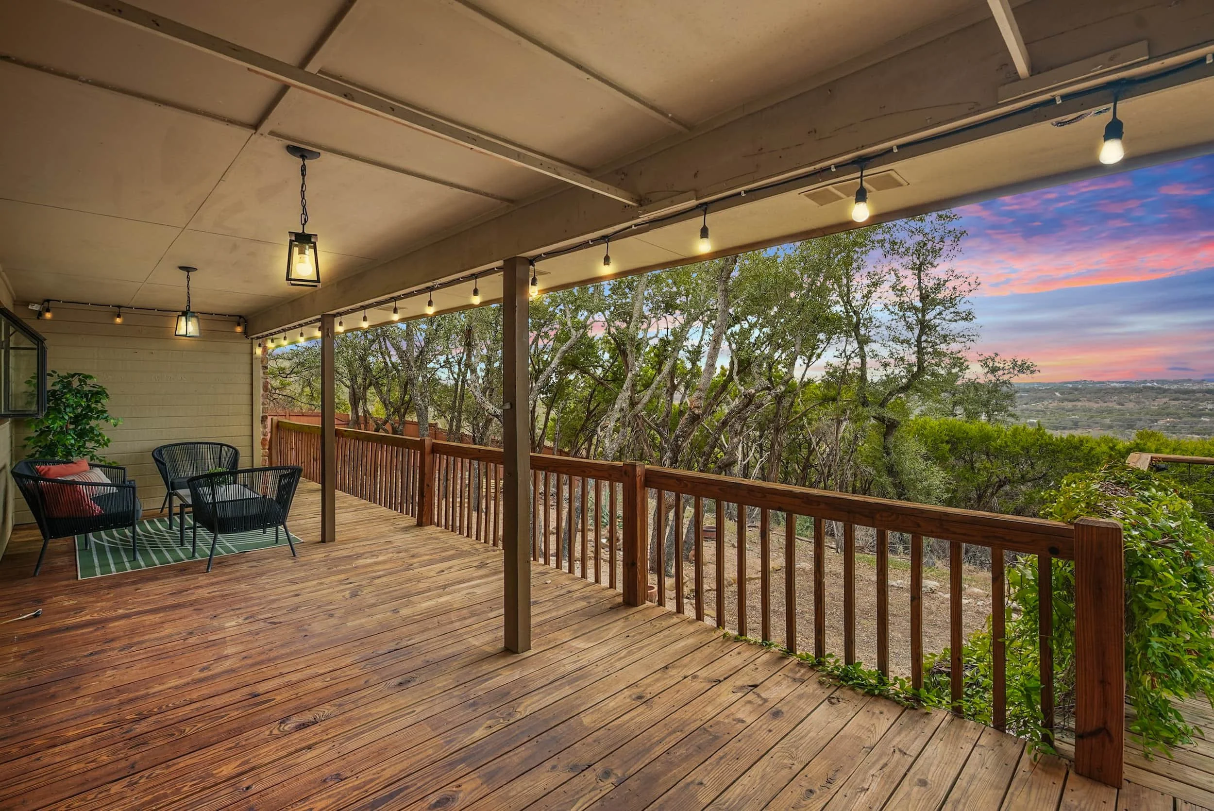 Inviting deck space on an Austin home overlooking greenery and distant hills at dusk with string lights, modern furniture, and warm wooden railings.