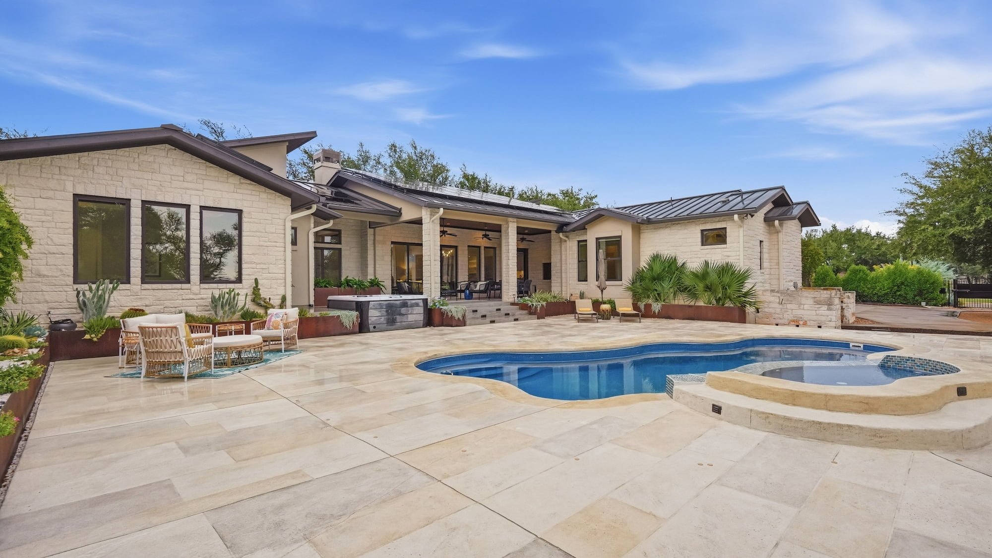 Backyard staged with rattan patio seating beside a freeform pool, spa, and limestone deck.