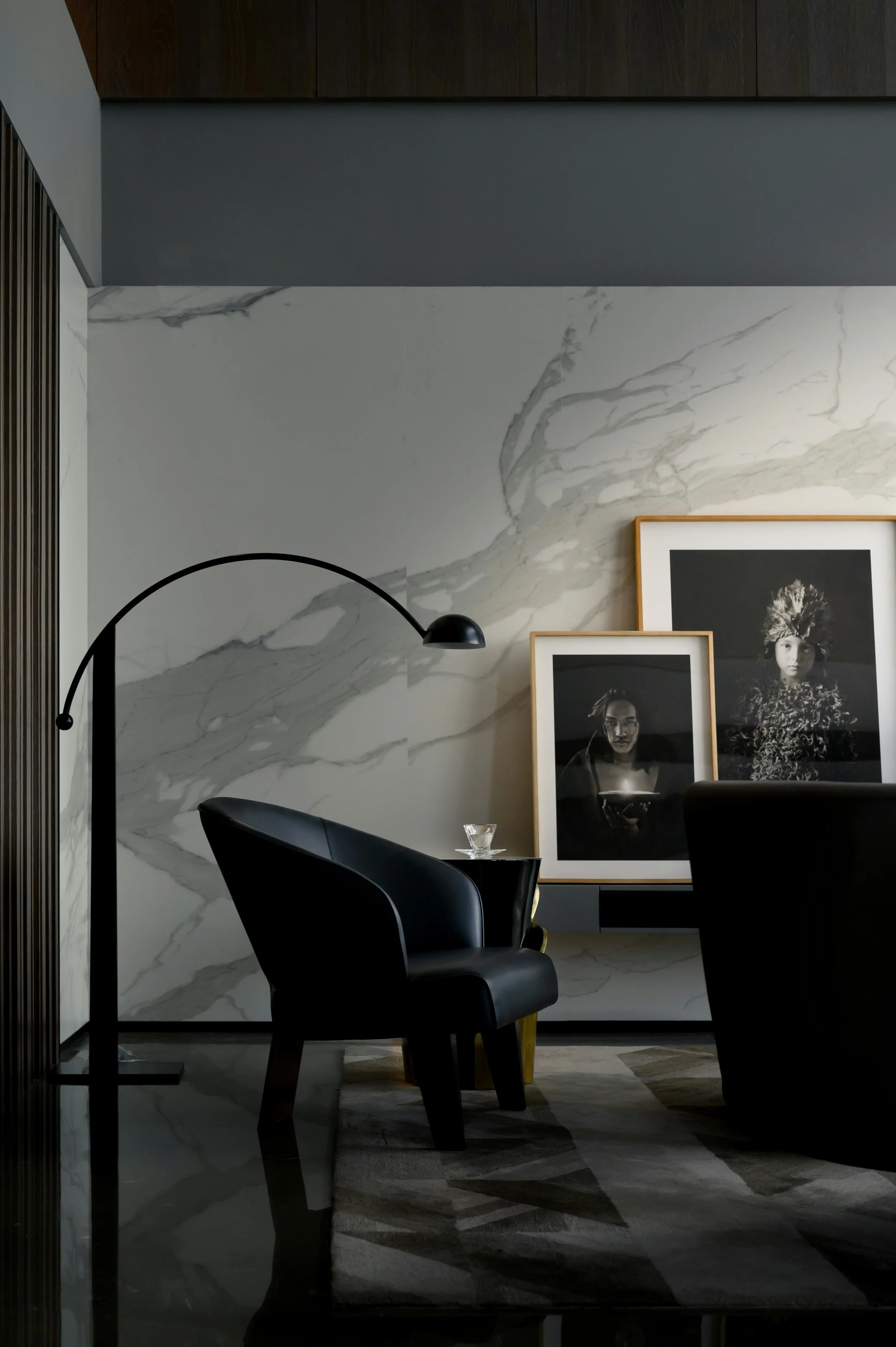 Moody luxury sitting room with marble accent wall, black leather chair, and arc floor lamp