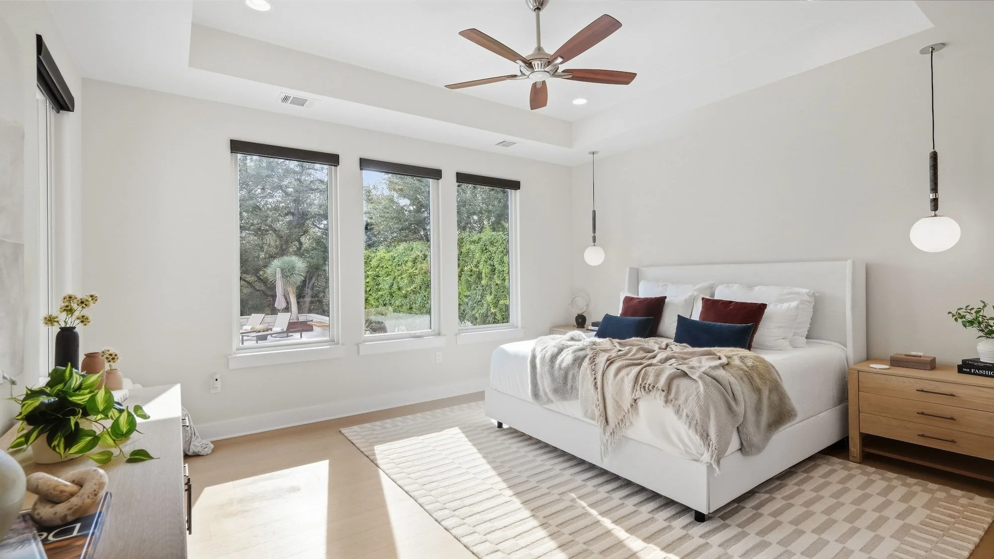 Bedroom staged with a white upholstered bed, layered throws, and globe pendants beside oak nightstands.