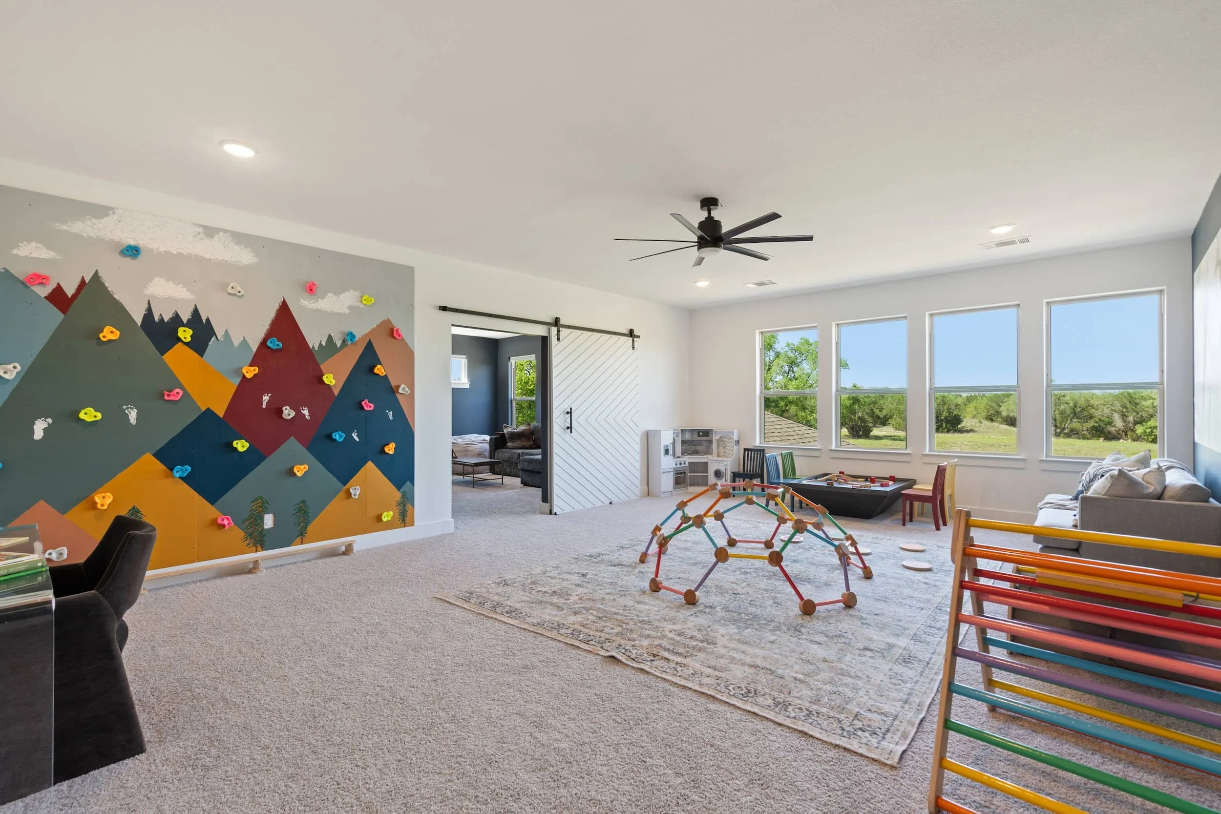 Austin home staging of modern playroom with climbing wall, soft carpet, colorful toys and bright natural light.