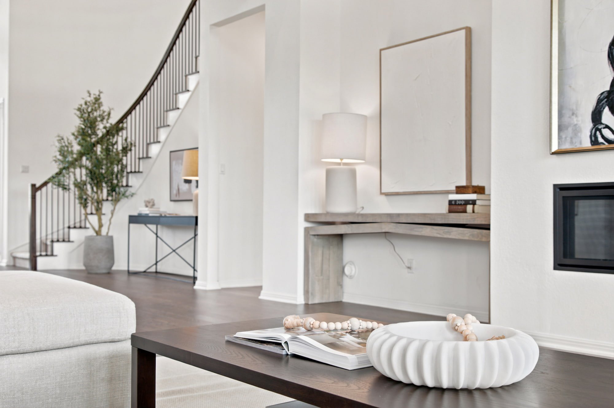 Styled books and a ribbed bowl top the coffee table, with the staircase visible beyond.
