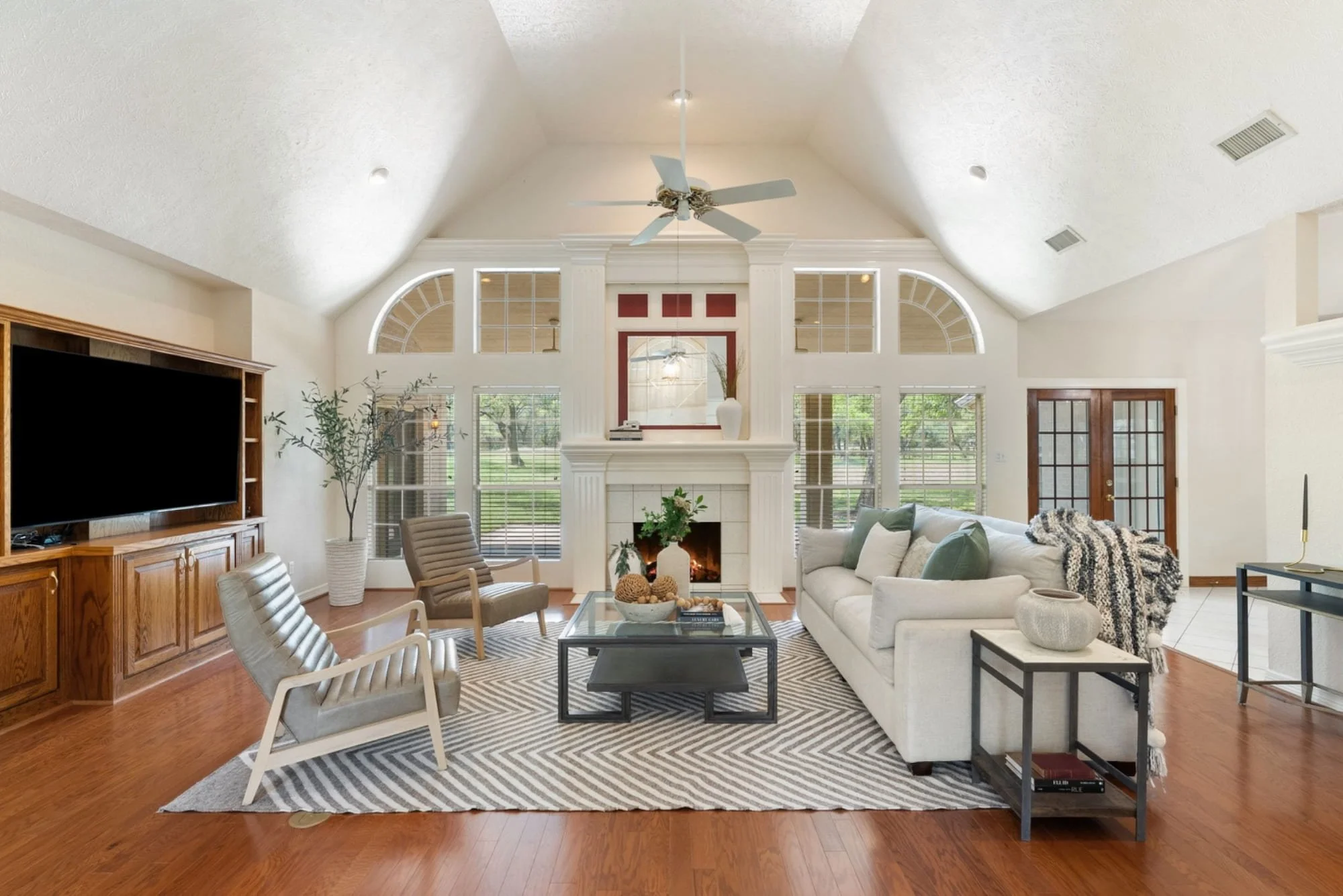 Living room with vaulted ceilings, hardwood floors, a fireplace, and large windows overlooking the backyard.